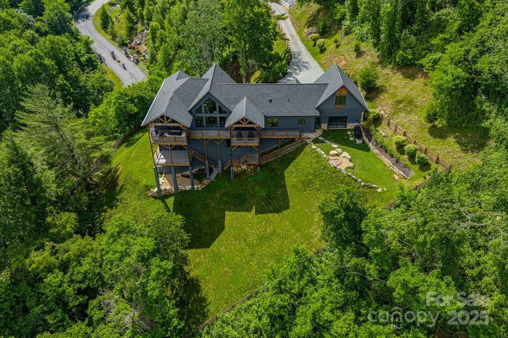 Aerial view of a dark-sided home with broad decks and lawn, surrounded by dense trees.
