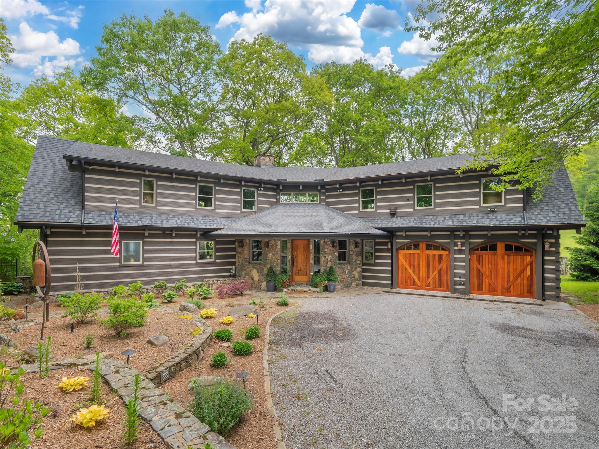Two-story home with stone entry, wooden garage doors, and landscaped garden beds.