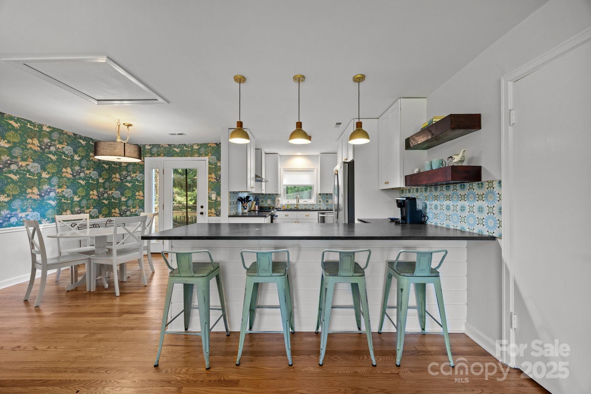 Kitchen and dining area with teal bar stools, patterned backsplash, and green floral wallpaper.