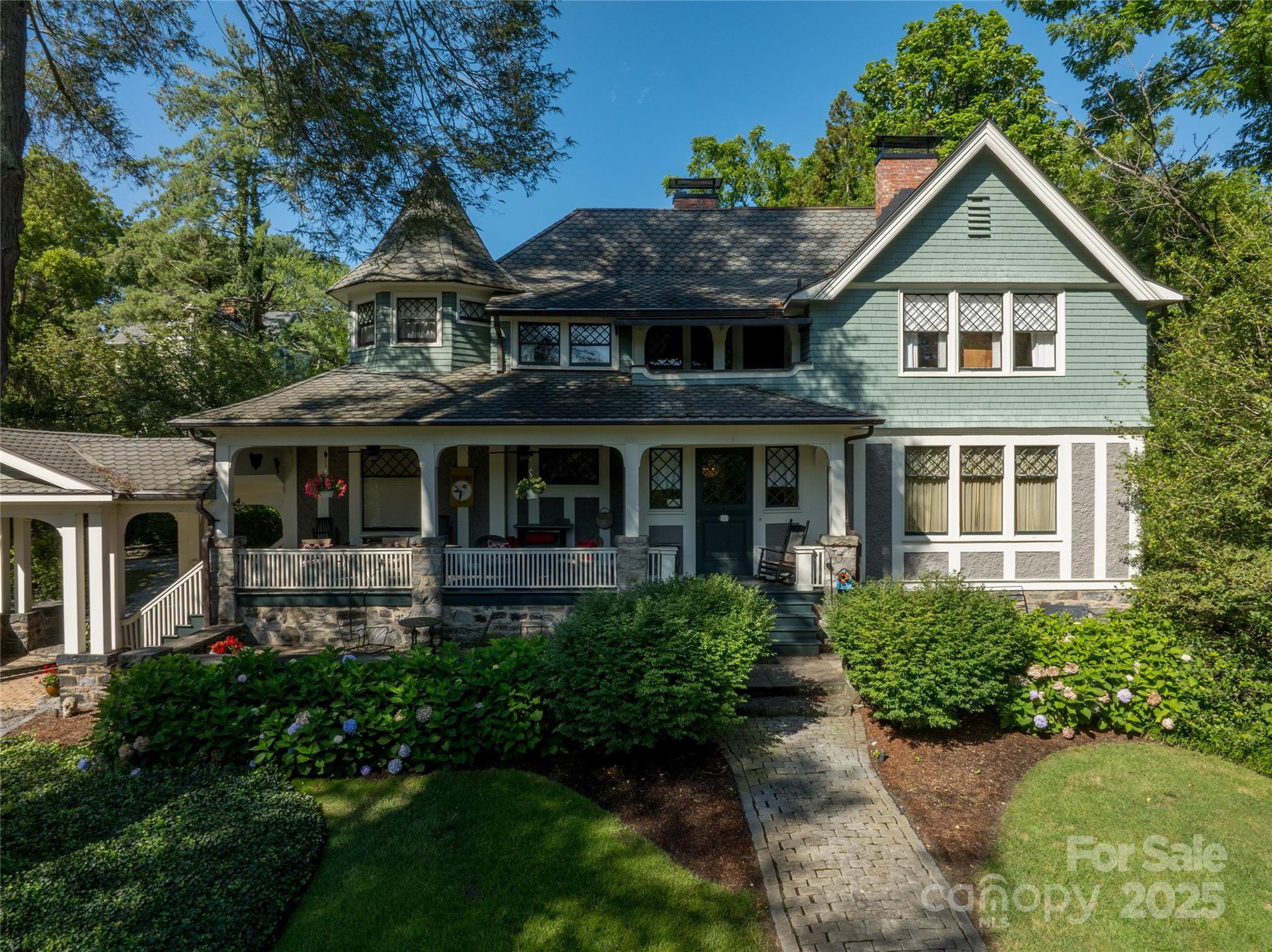 Green two-story house with a covered porch, turret, and landscaped front garden.