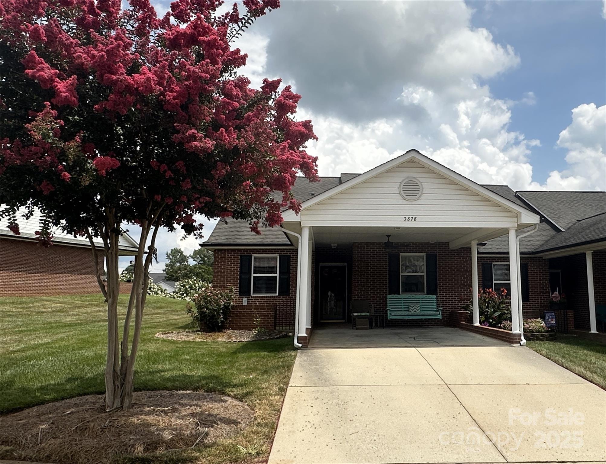 Brick townhome with a covered porch and driveway, framed by a large pink-flowering tree.