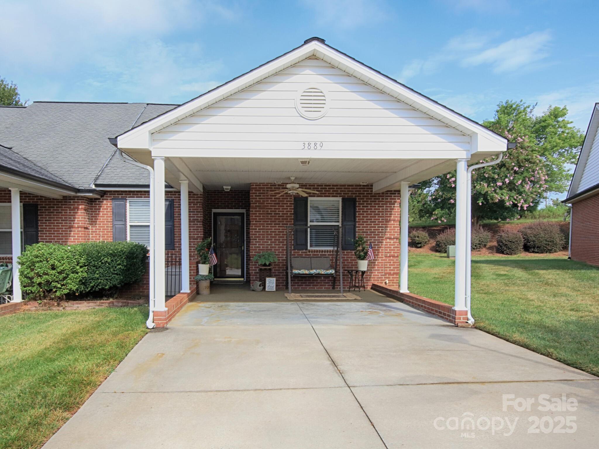 Red-brick townhome with a covered driveway and furnished front porch.