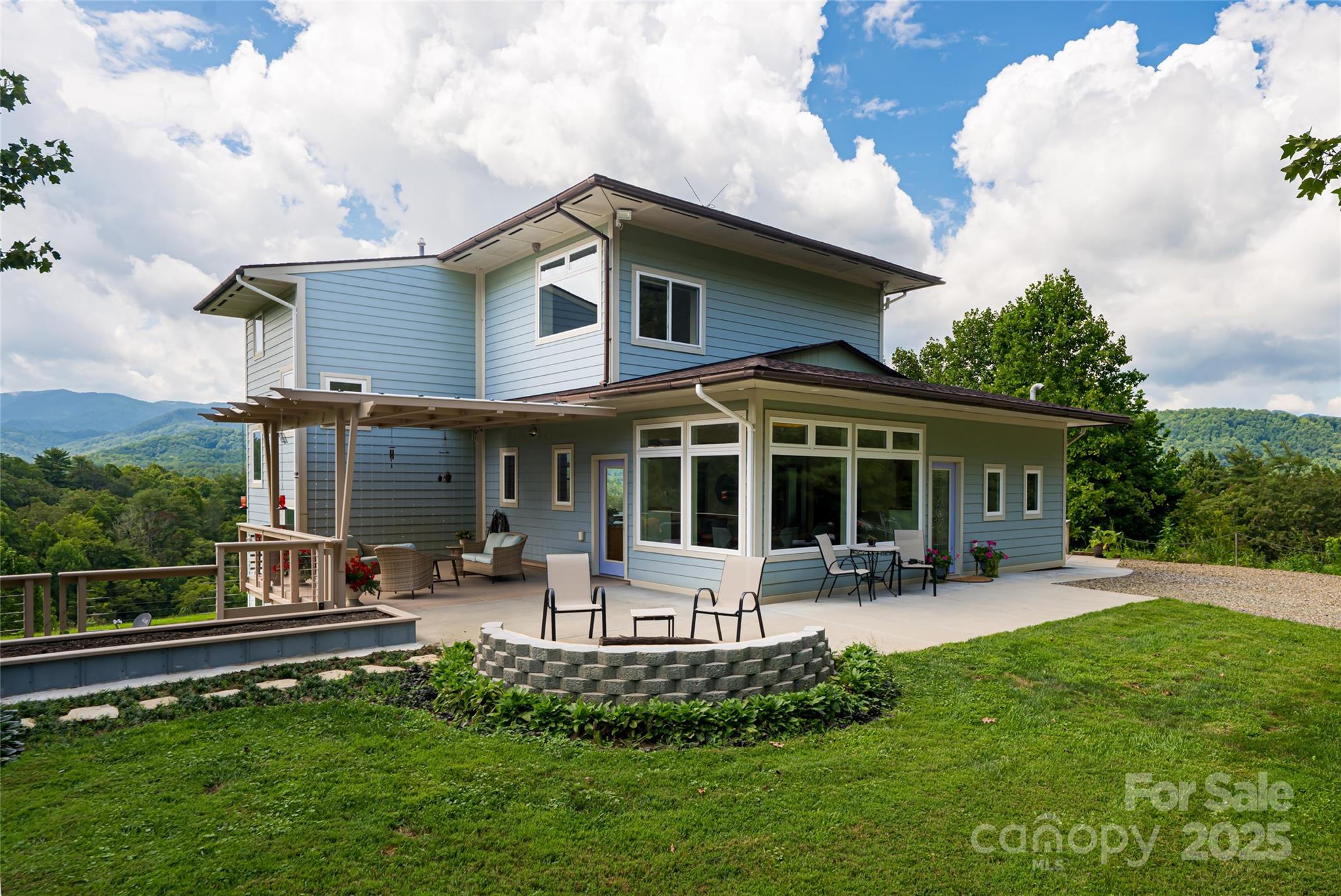 Blue two-story home with a spacious patio, green lawn, and forested mountain views.