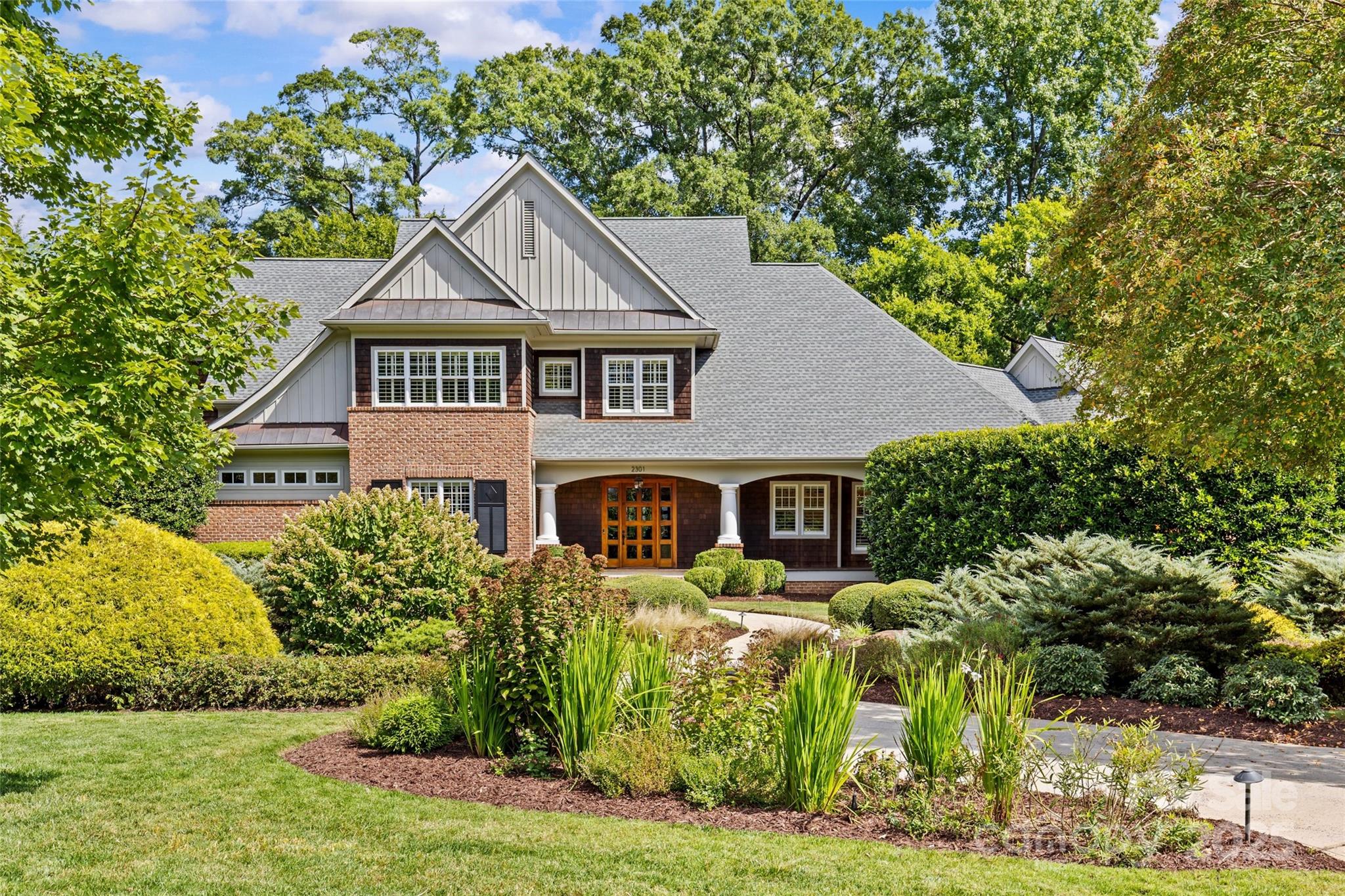 Large brick-and-shingle home with a covered entry, gabled roof, and landscaped front garden.