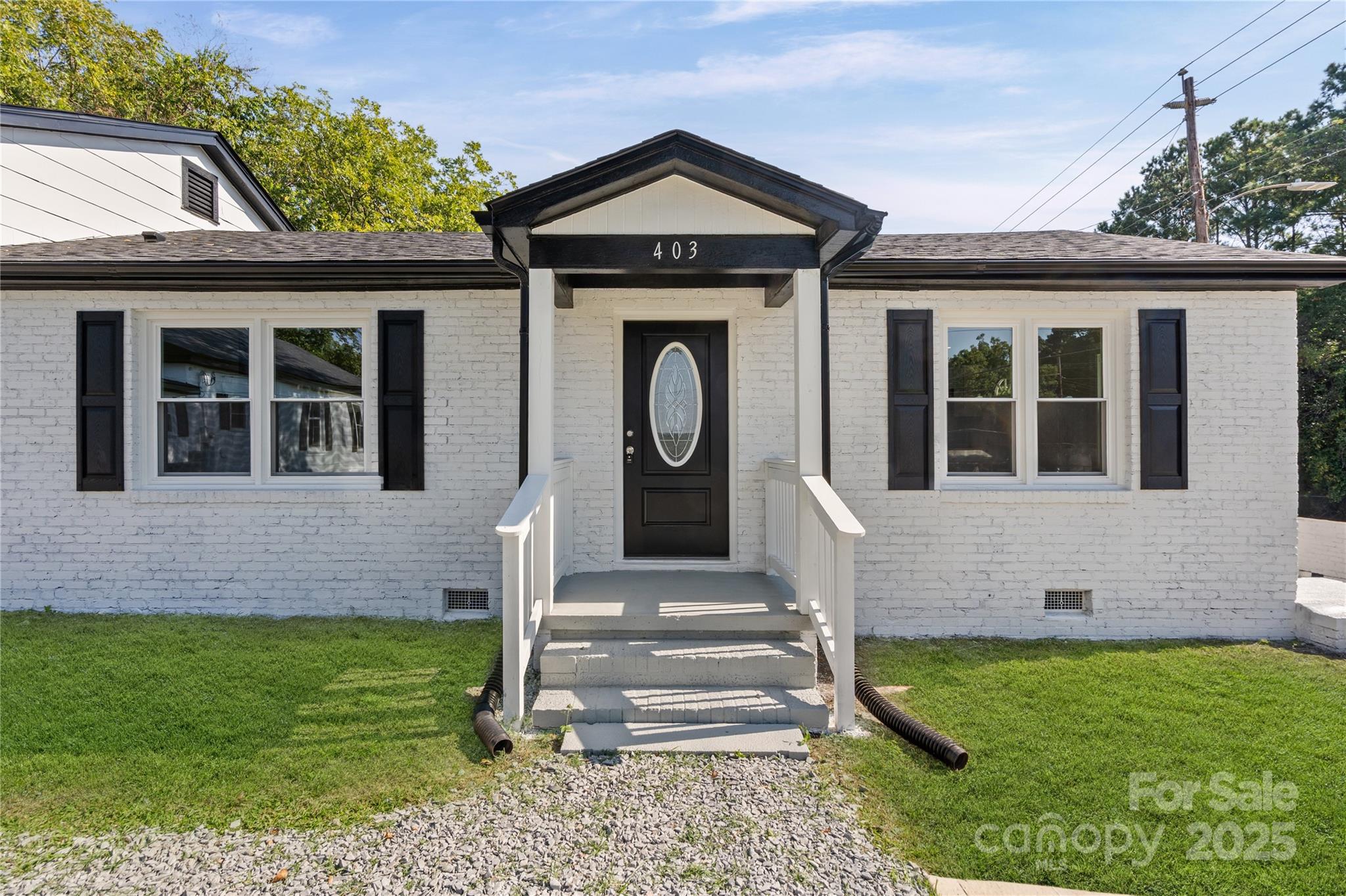 White brick house with black trim, a centered gabled entry, and steps leading across a gravel path.