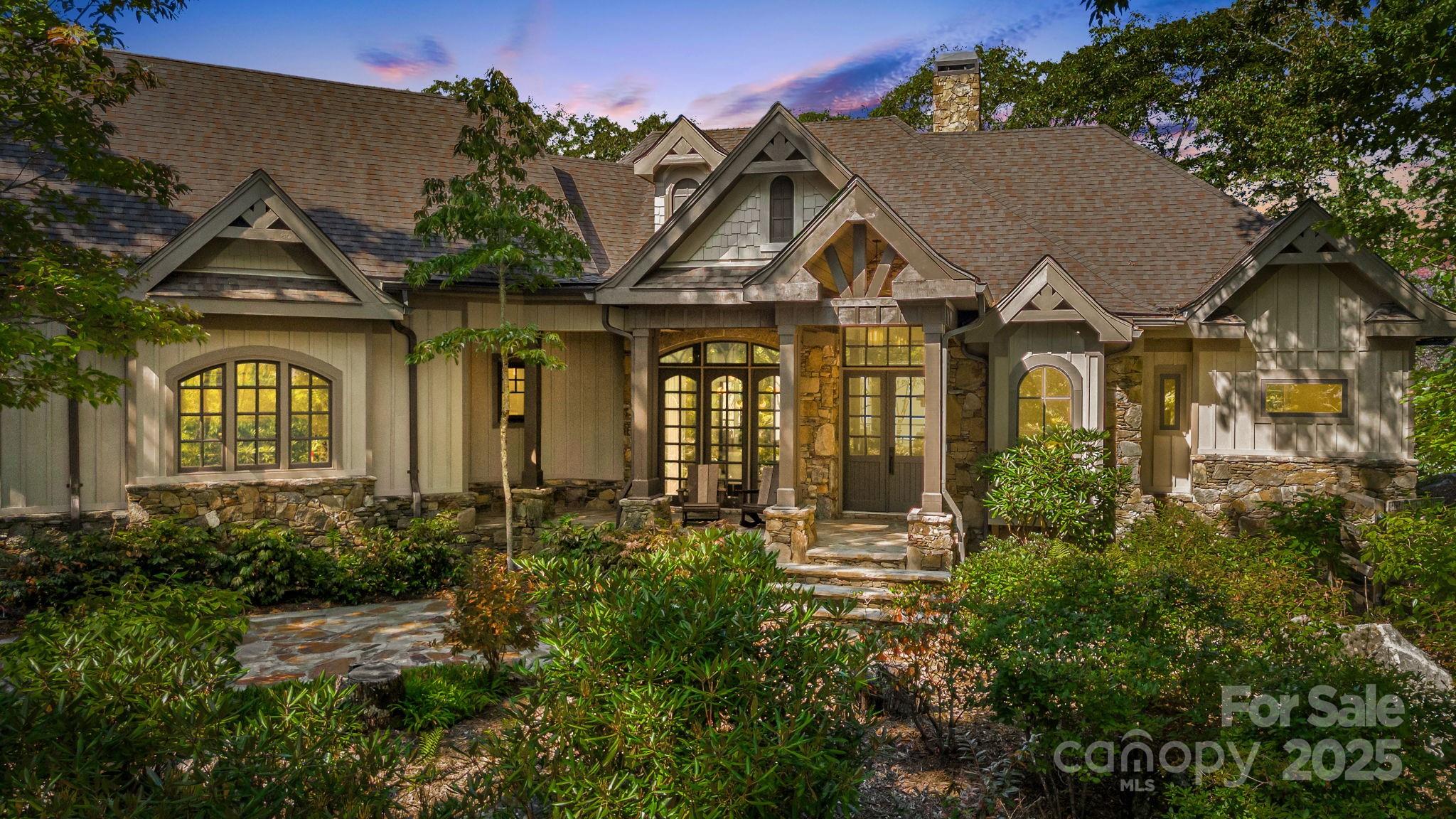 Craftsman-style home with stone accents, peaked gables, and lush landscaping at dusk.