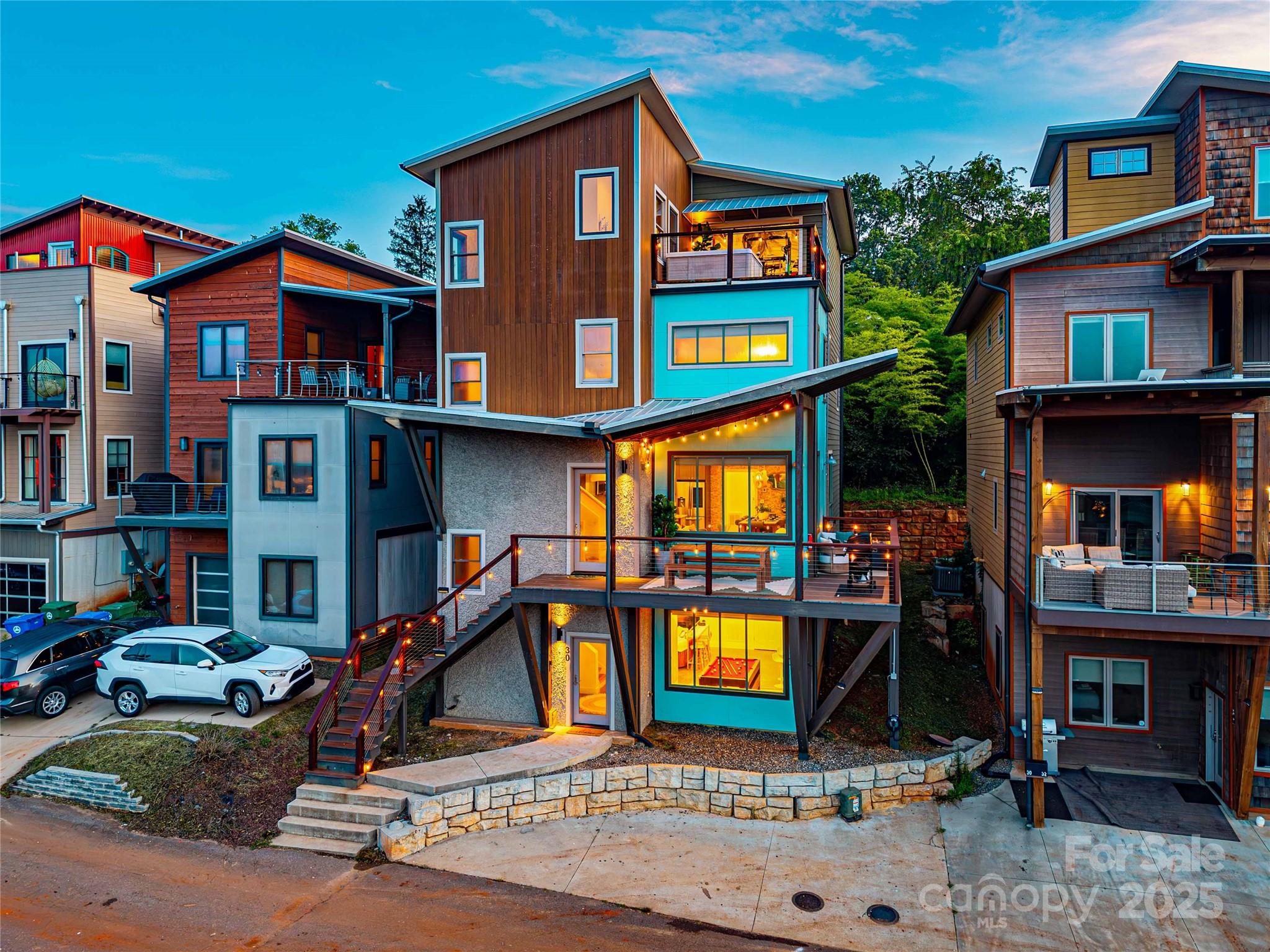 Modern multilevel home with turquoise siding, illuminated windows, and decks at dusk.