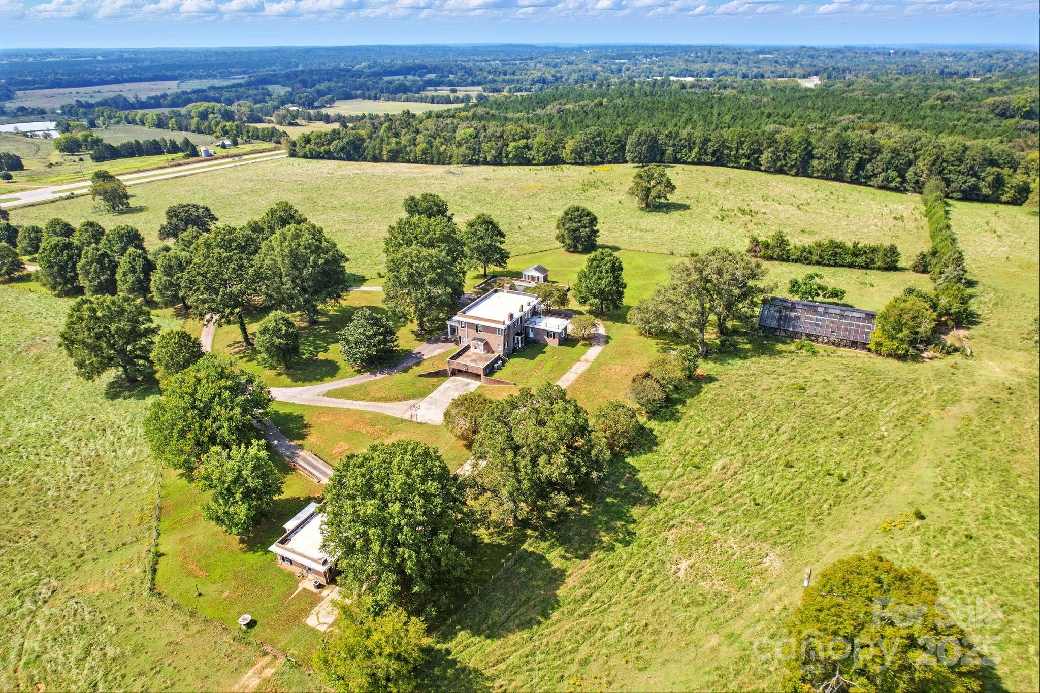 Aerial view of a brick house, outbuilding, and broad pasture surrounded by mature trees.
