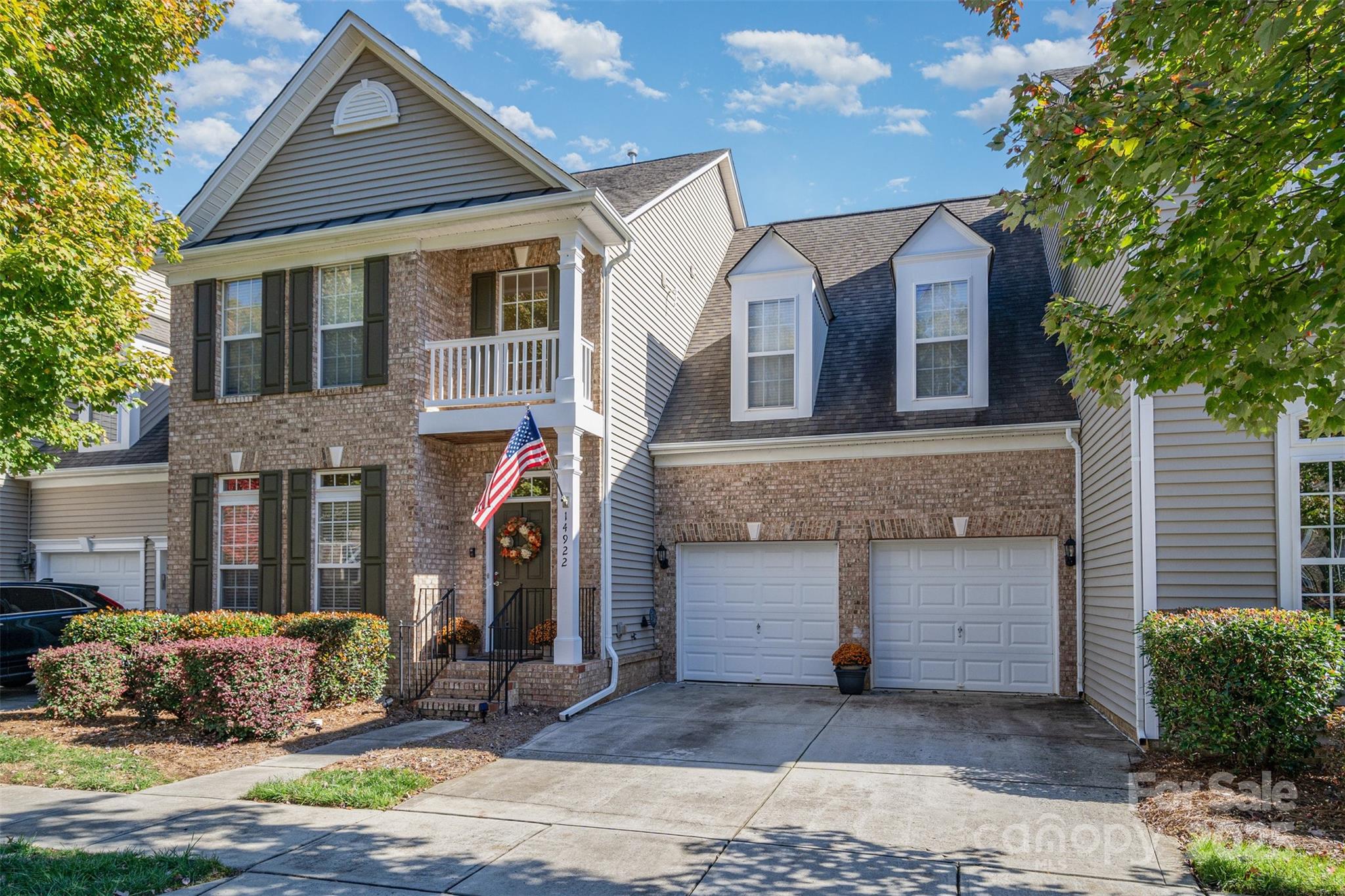 Attached brick-and-siding townhome with two garage doors, a balcony, and an American flag.