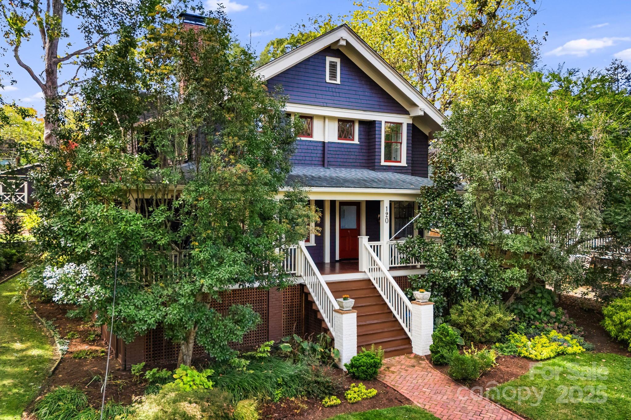Dark blue two-story house with a red front door, white-railed staircase, and leafy garden.