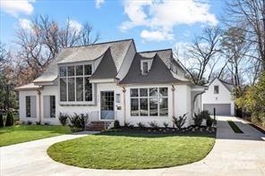White house with dark gabled roofs, large windows, and a curved front lawn.