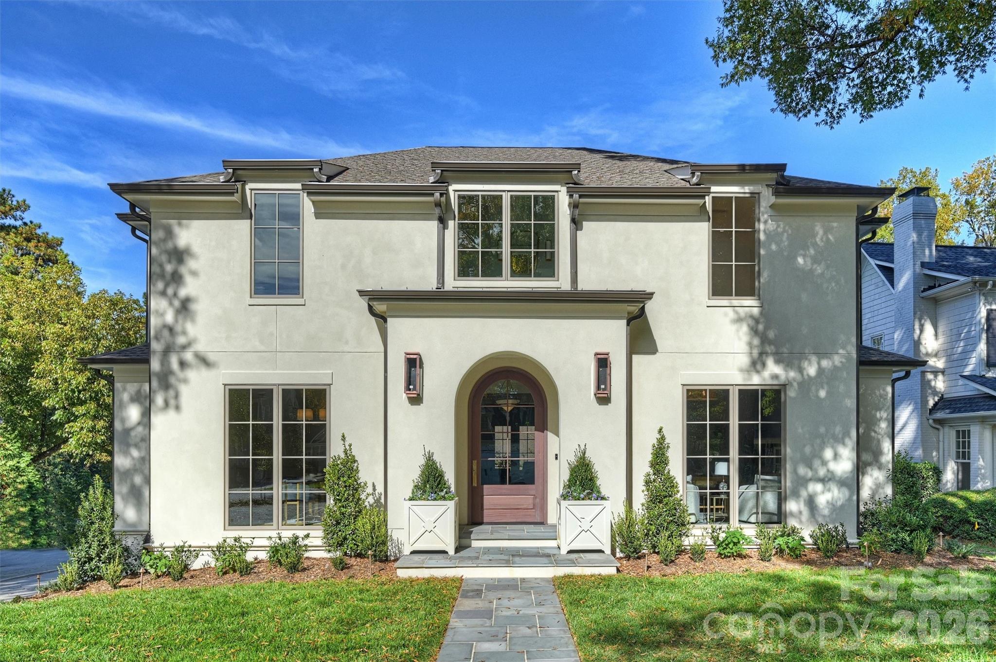 Two-story home with a prominent arched entry, tall windows, and landscaped front yard.