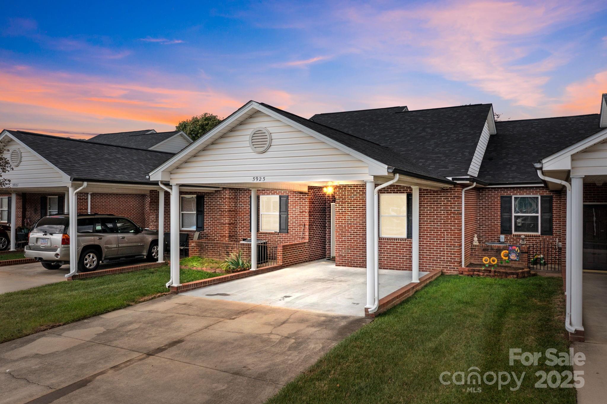 Brick townhomes with covered carports and a parked SUV beneath a colorful sunset sky.