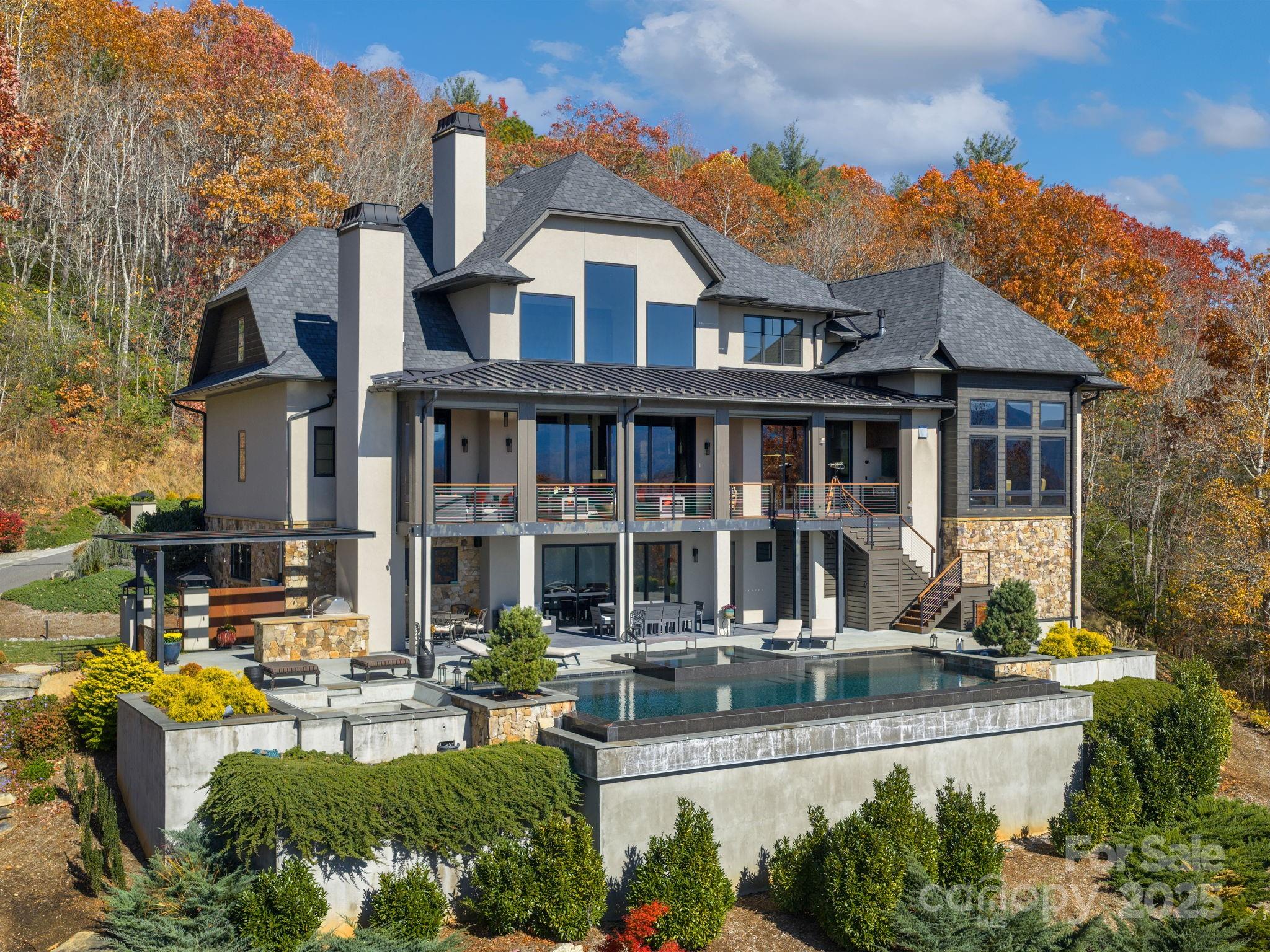 Modern multi-story home with covered decks and a pool, surrounded by autumn foliage.