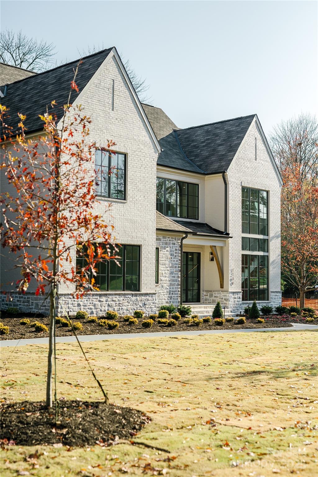 Two-story white brick home with gray stone accents, black-framed windows, and autumn trees in front.