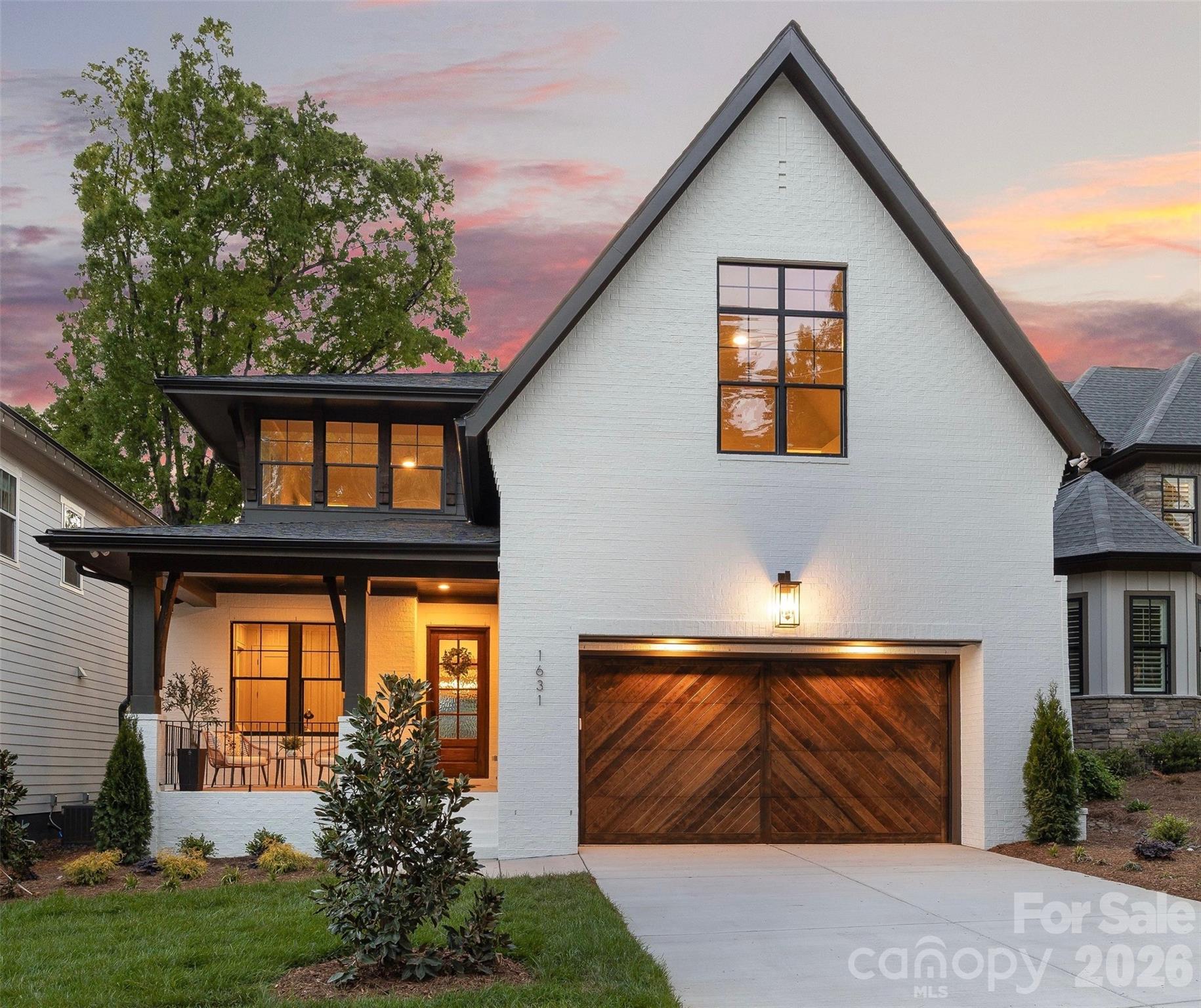 White-brick house with a steep gable roof and wood garage door, warmly lit at dusk.