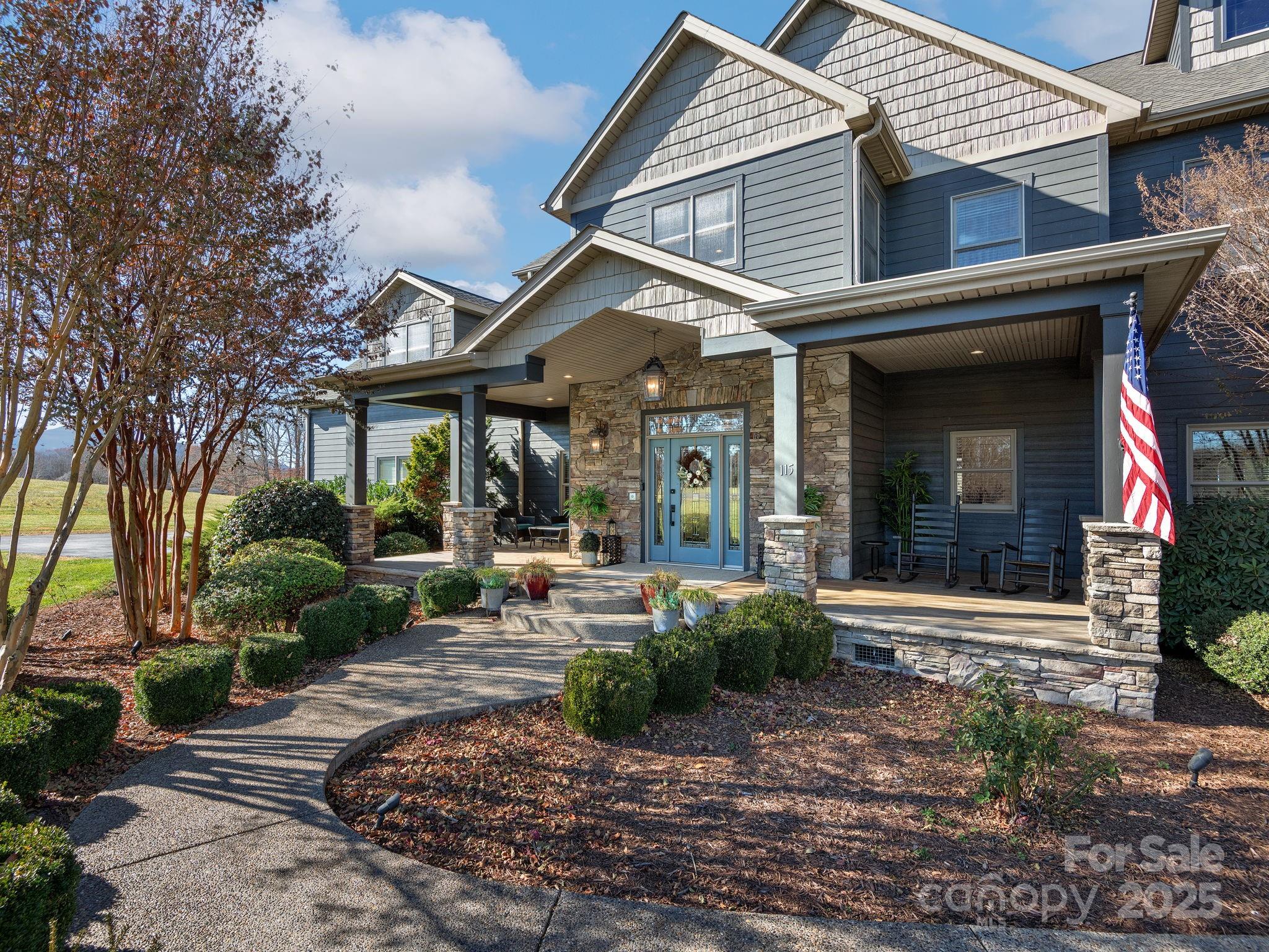 Blue-gray two-story home with a stone-accented covered porch, landscaped front yard, and American flag.
