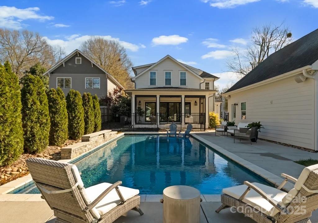 Backyard pool with lounge chairs, patio seating, and a covered porch.