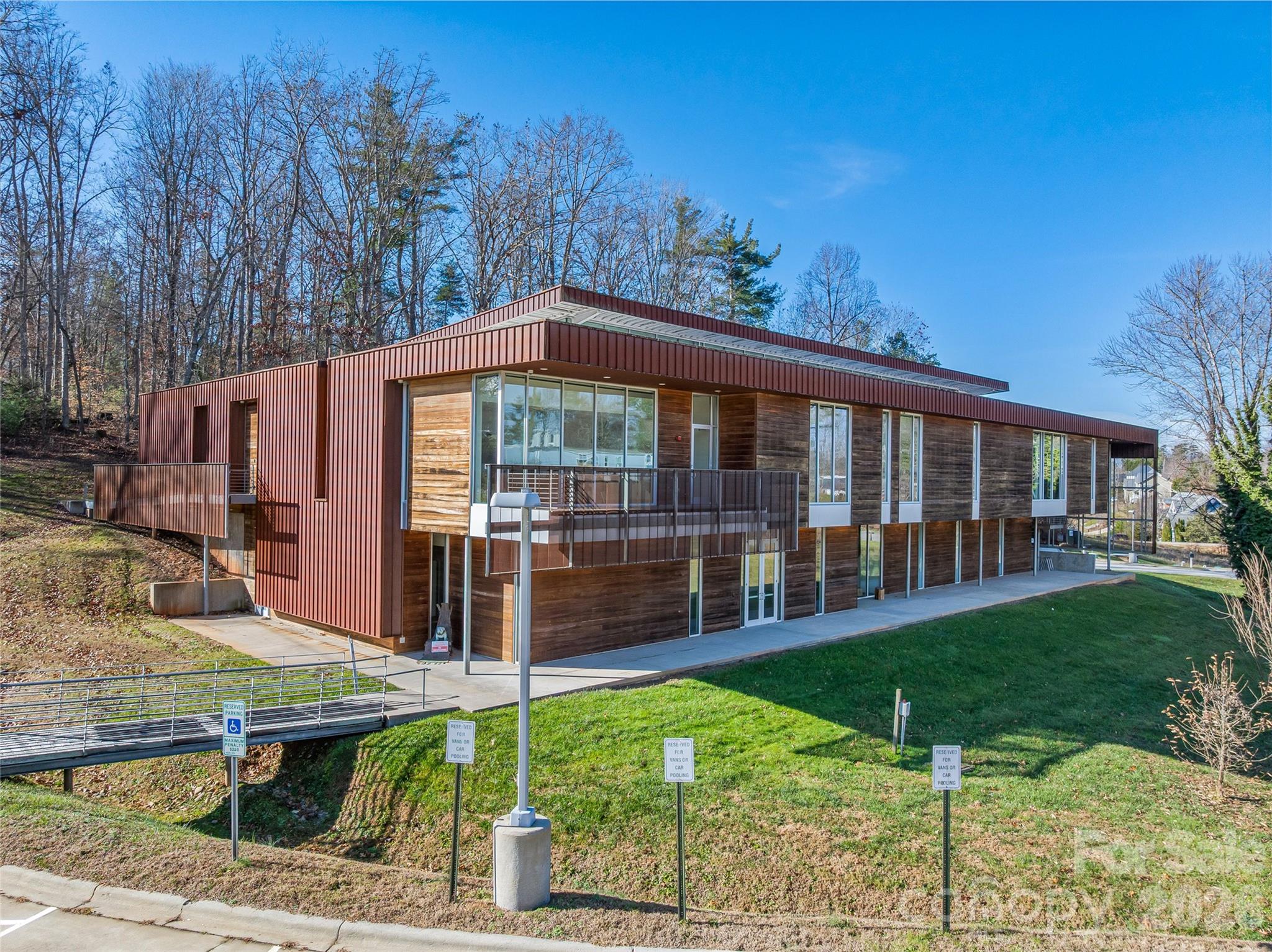 Modern two-story building with red metal siding, wood walls, and broad windows on a grassy lot.