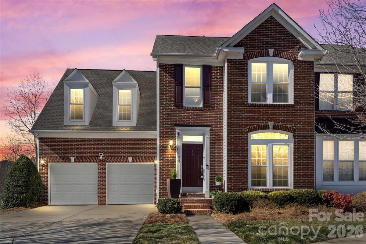 Two-story brick home with a double garage and warmly lit windows at dusk.