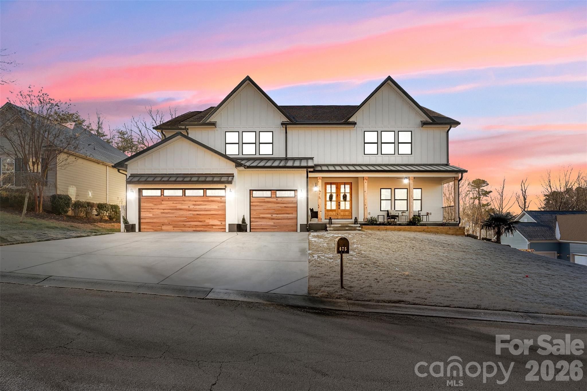 Two-story white farmhouse with twin wood garage doors and a covered porch beneath a pink dusk sky.