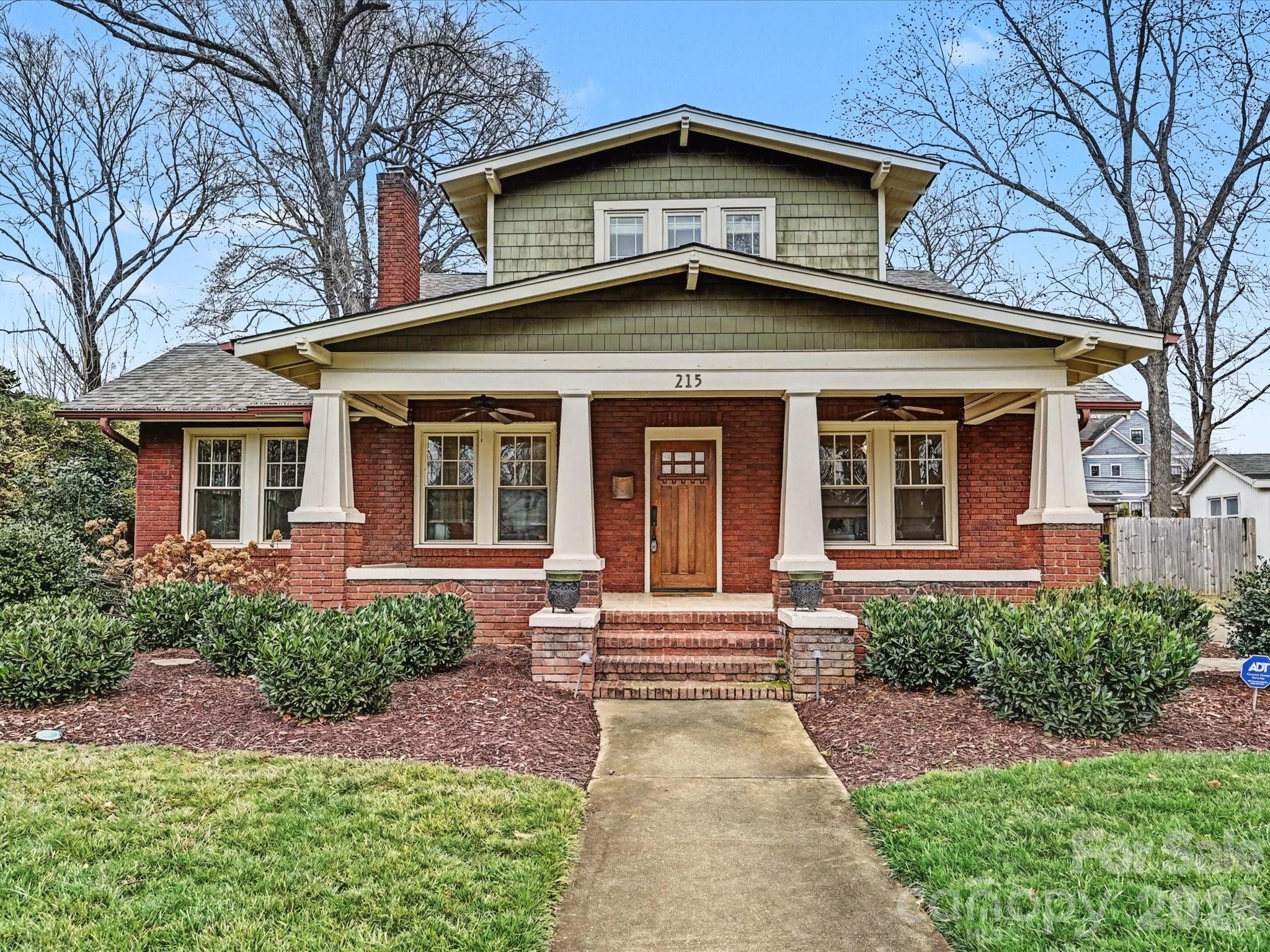 Red brick house with a broad covered porch, white columns, and a walkway to the front steps.