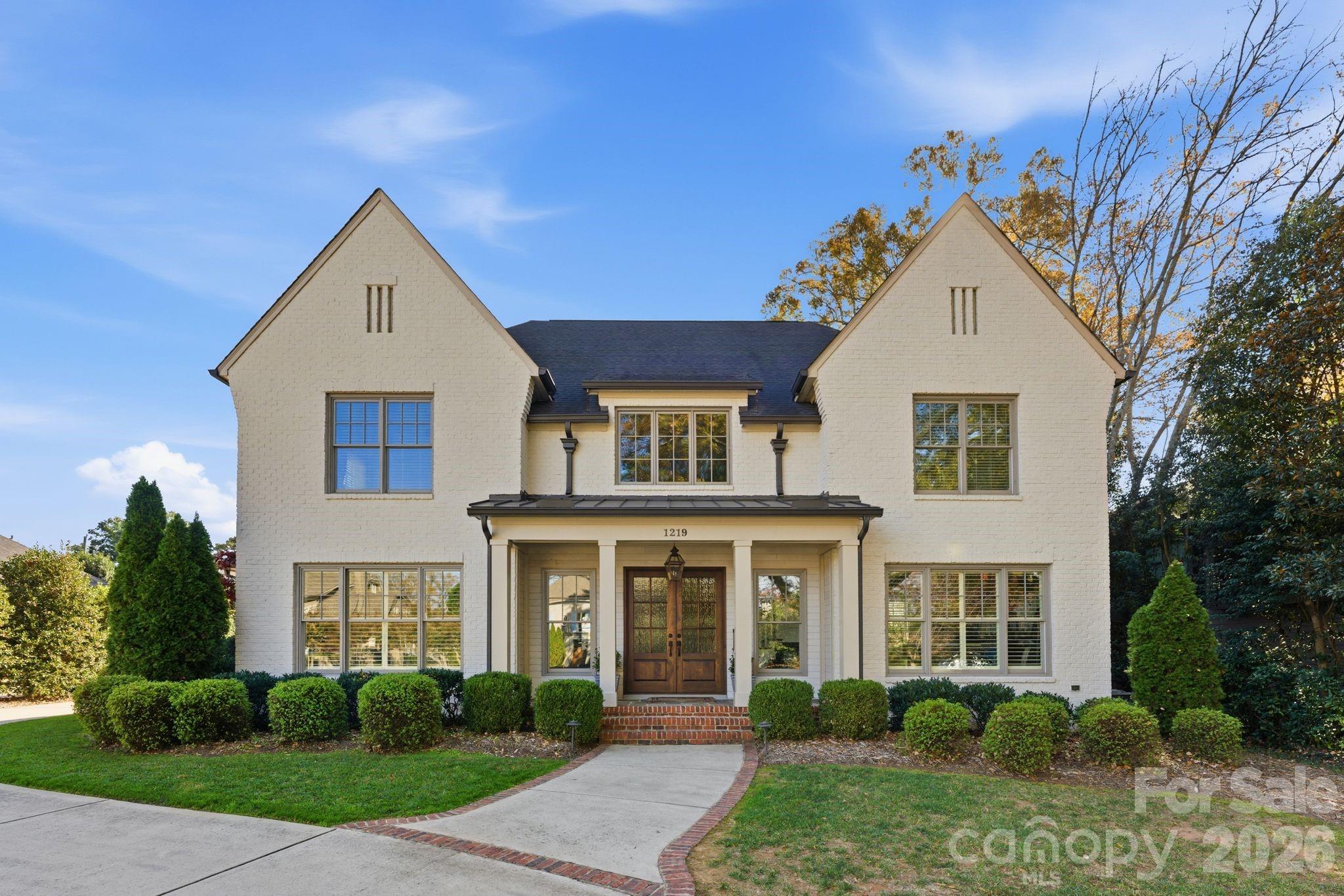 White brick two-story house with twin gables, a columned entry porch, and a curved walkway.