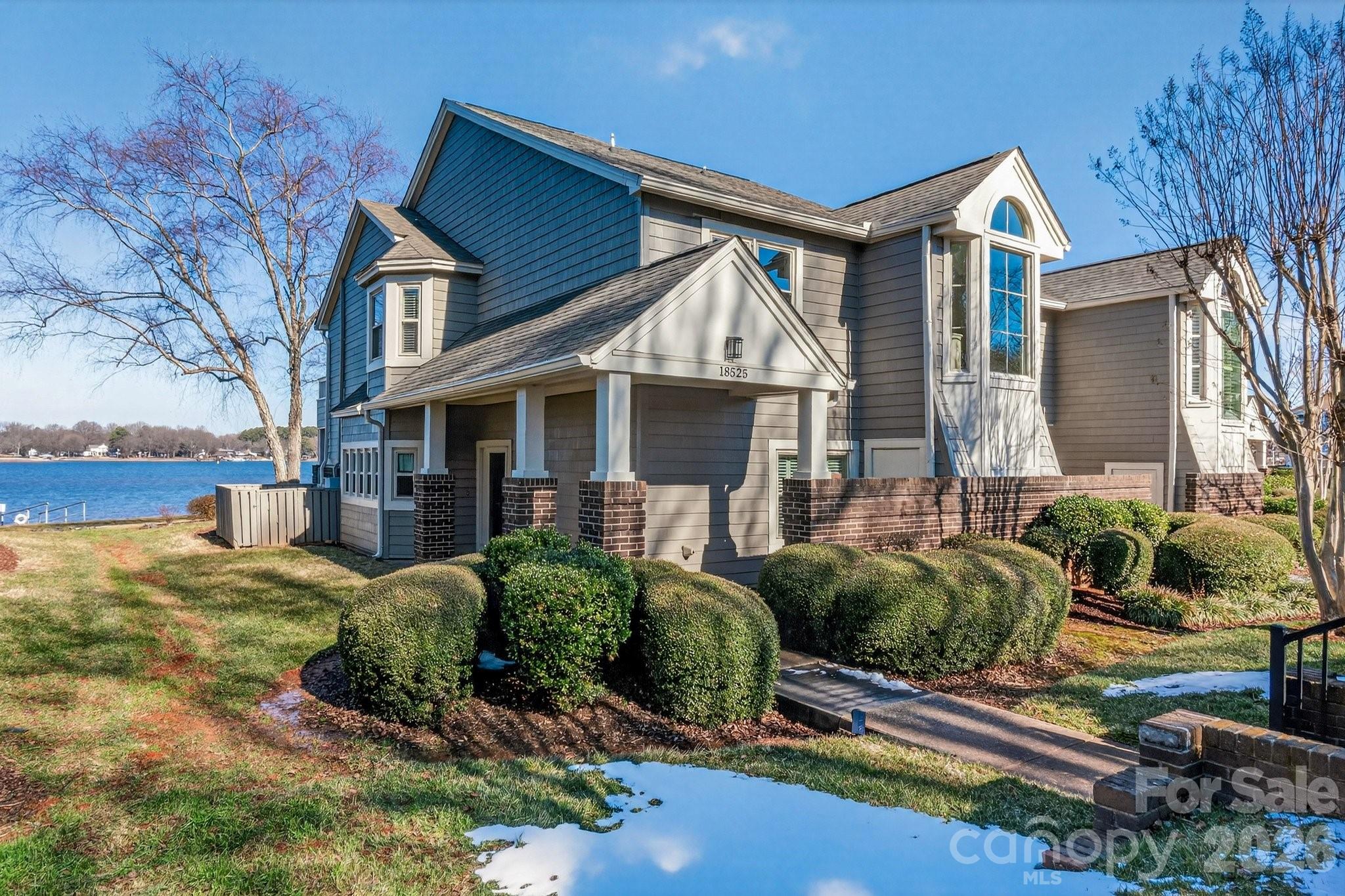 Gray lakeside condo building with blue siding, brick porch supports, and landscaped shrubs.
