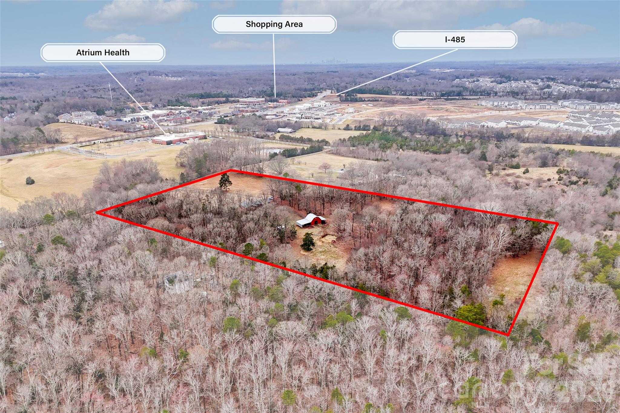 Wooded property outlined in red, with a small barn and nearby development visible from above.