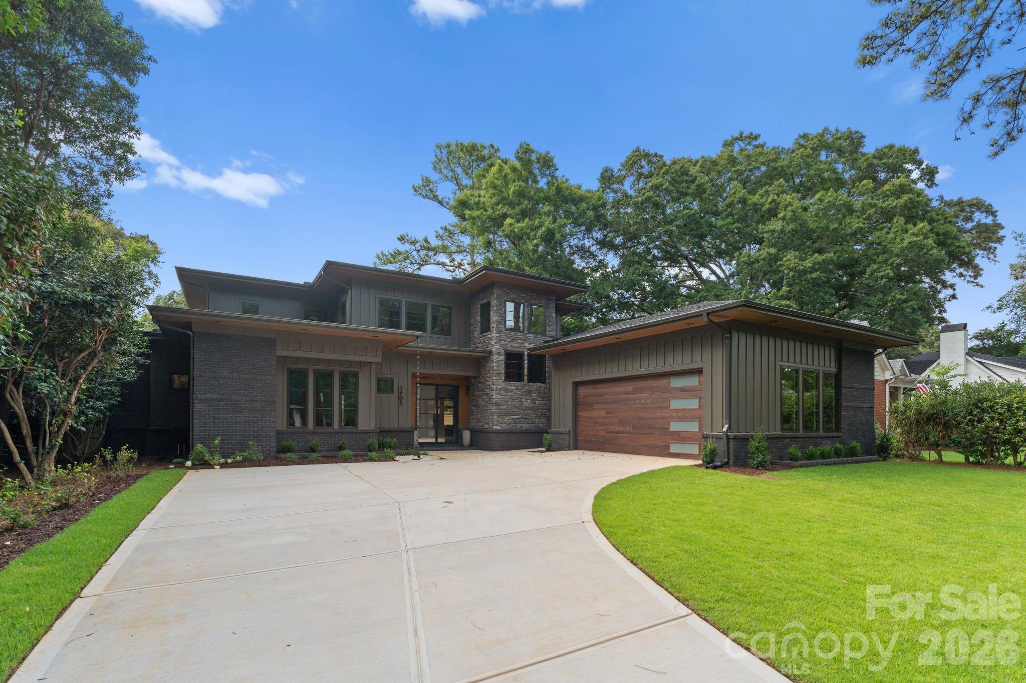 Contemporary two-story home with stone accents, a wide wooden garage door, and a curved driveway.