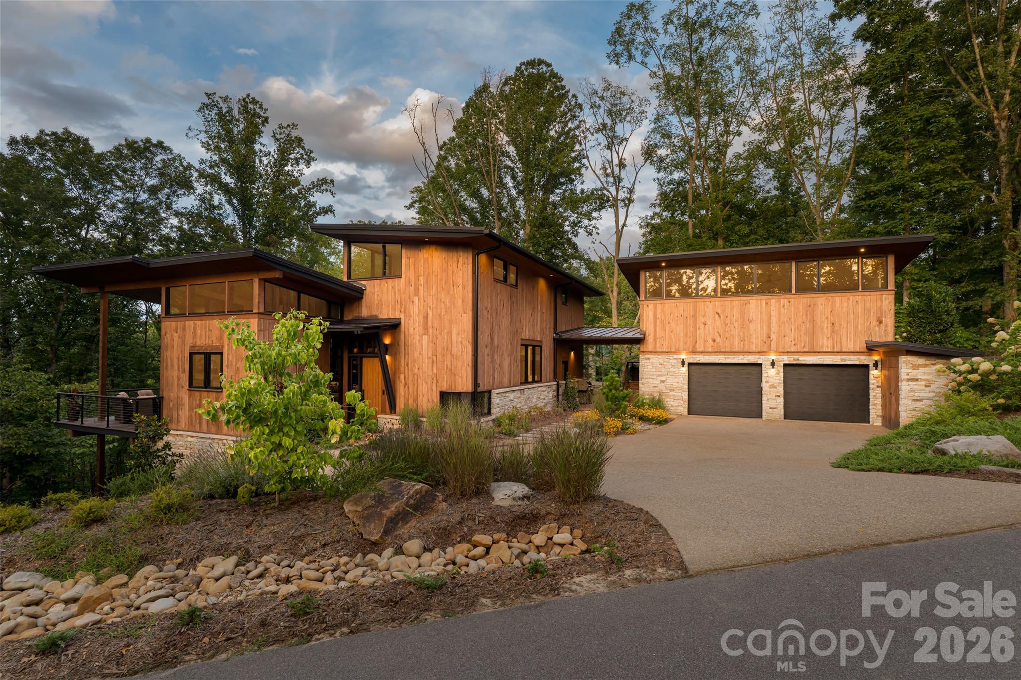Contemporary wood-sided home with stone accents, a two-car garage, and mature trees.