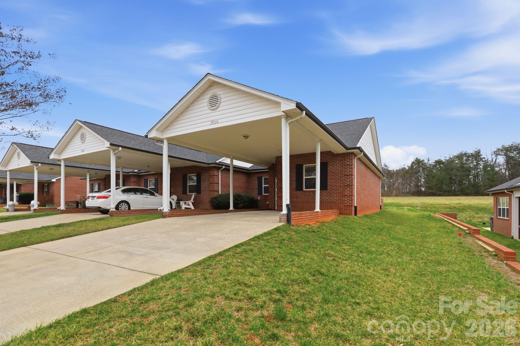 Brick townhome with a covered carport, concrete driveway, and white car parked out front.