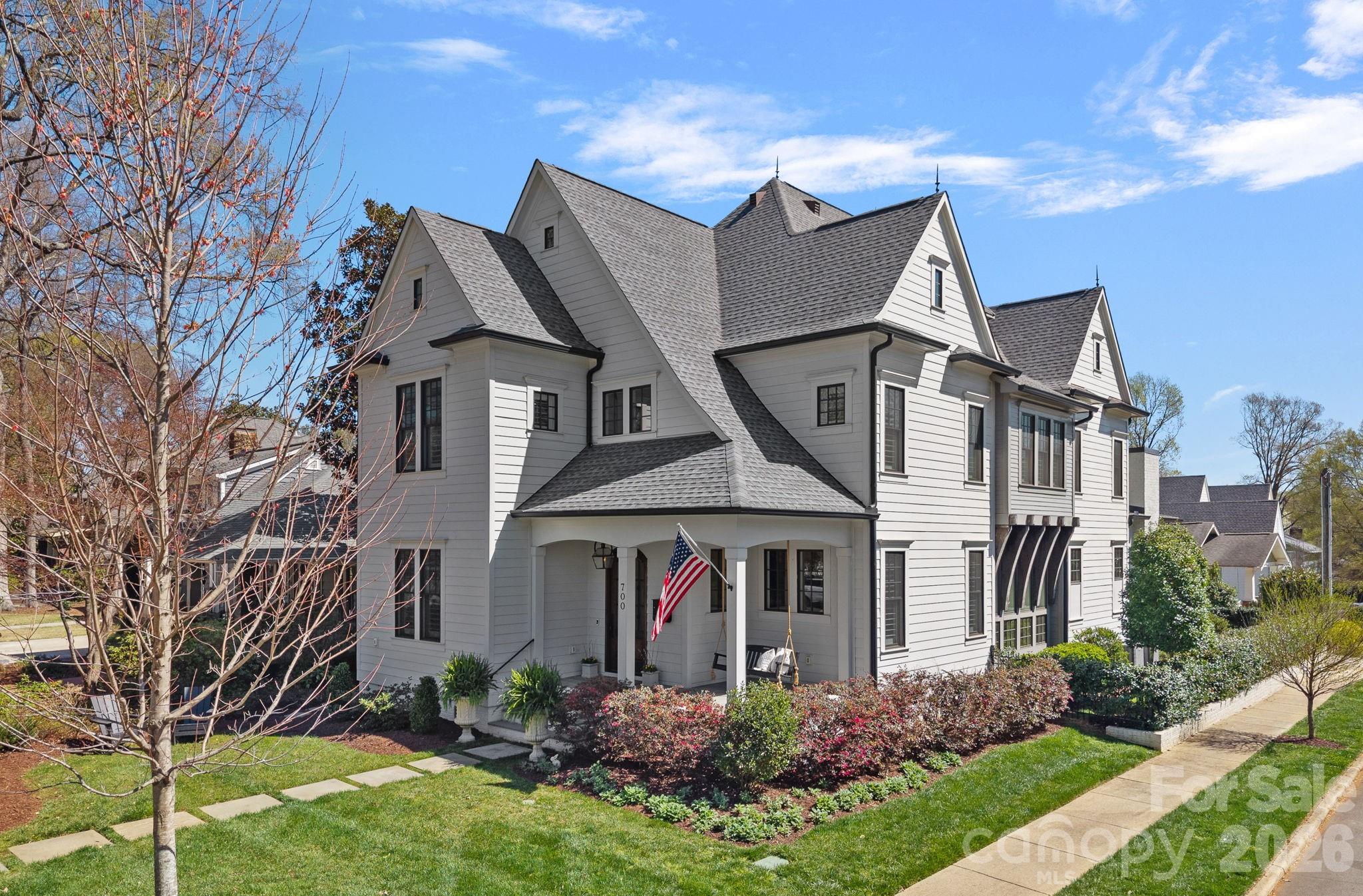 Large white clapboard house with steep gray gables, a covered porch, and an American flag.