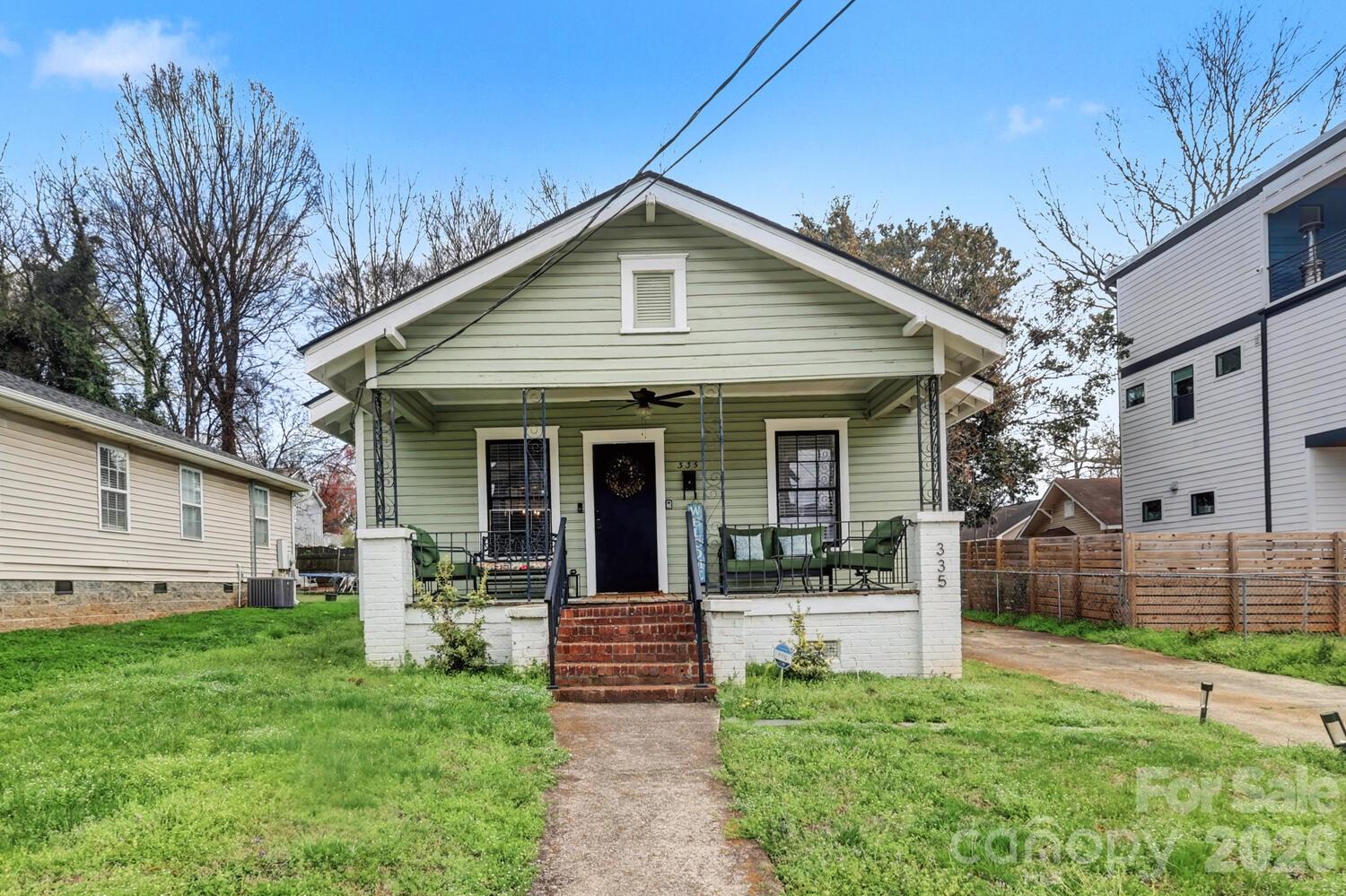 Pale green house with a covered porch, black front door, and brick steps.