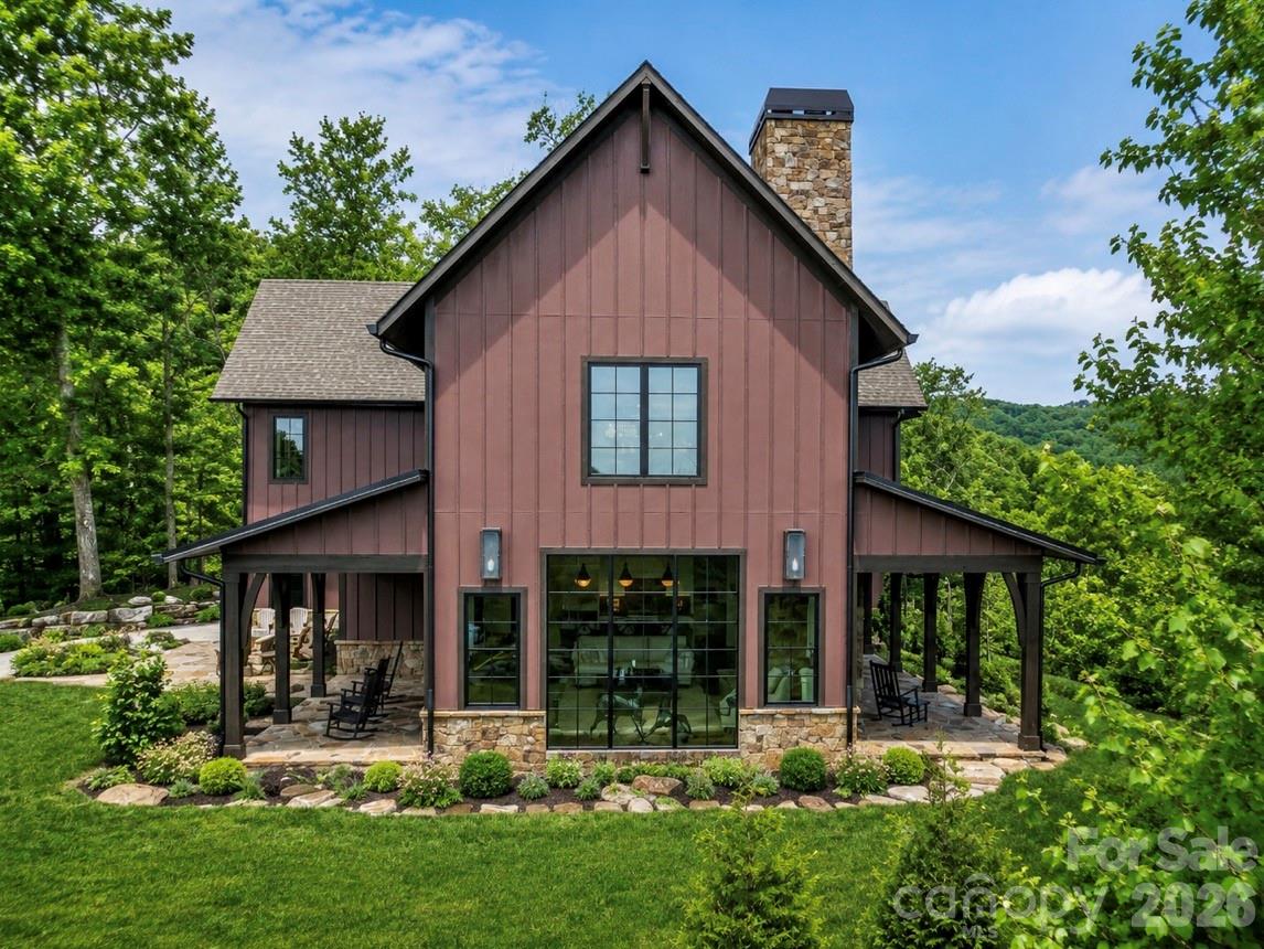 Two-story red-sided home with stone accents, covered patios, and a landscaped yard among trees.