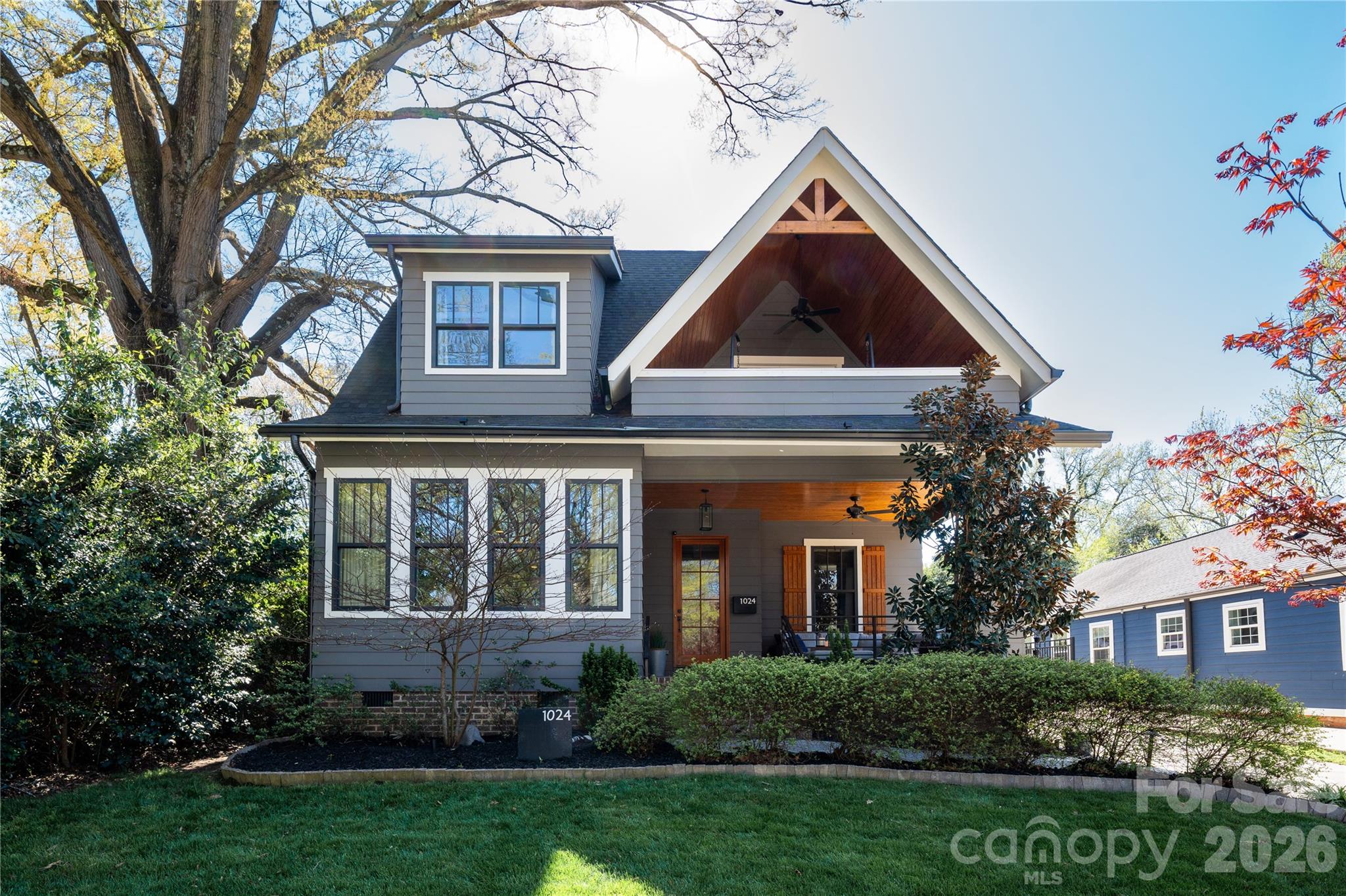 Gray two-story house with a timber-accented gable, covered porch, and mature trees.