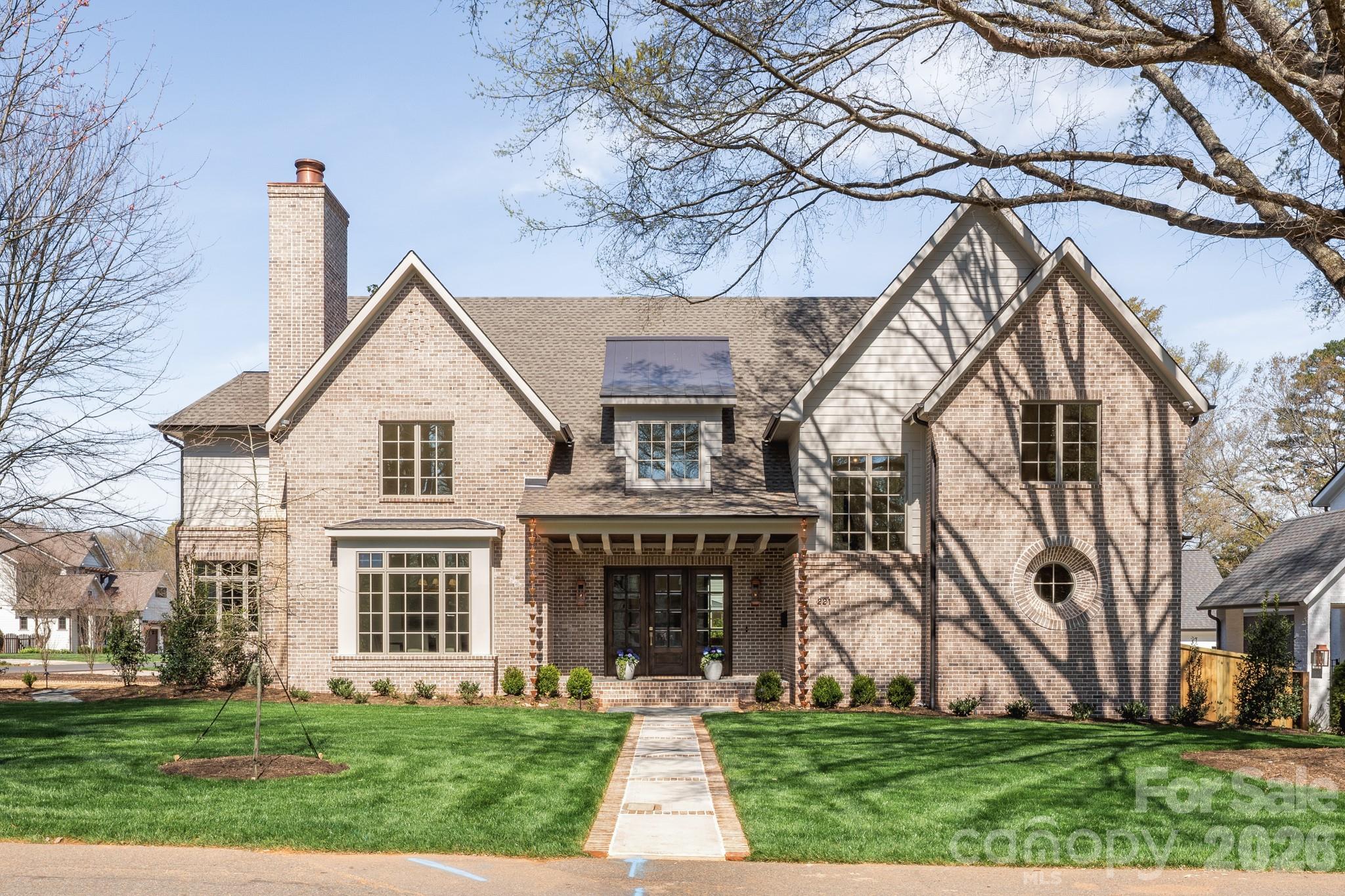 Two-story brick house with multiple gables, a circular window, and a walkway across the front lawn.
