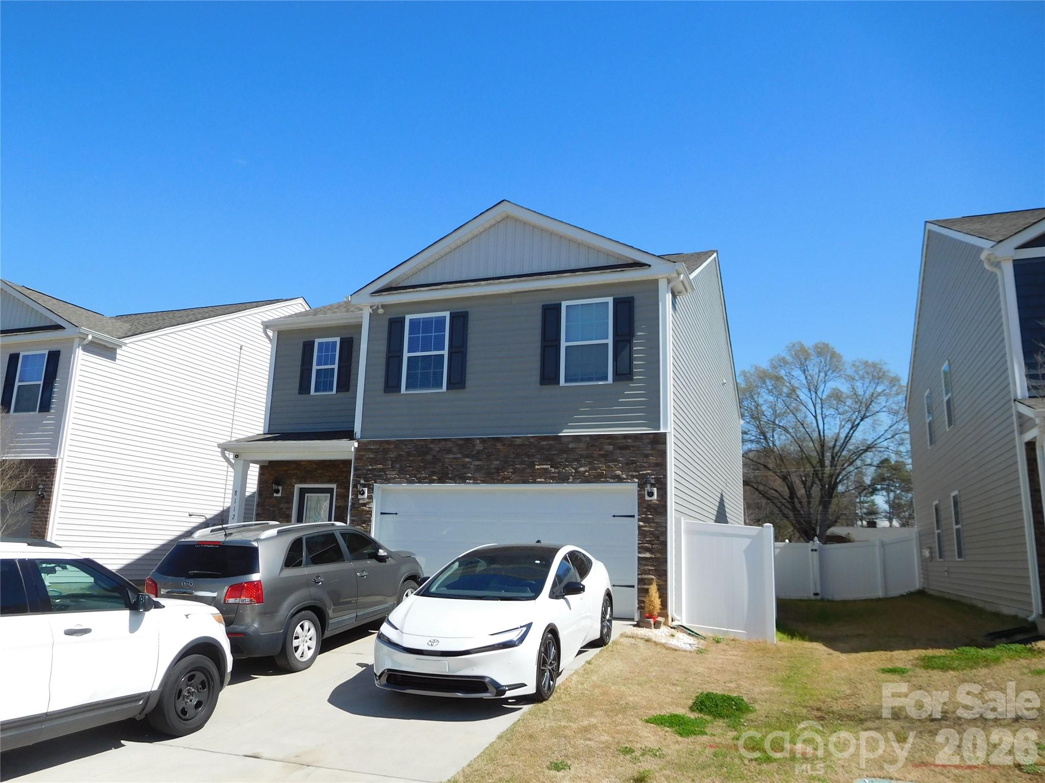 Two-story gray house with a stone facade, white garage door, and cars parked in the driveway.