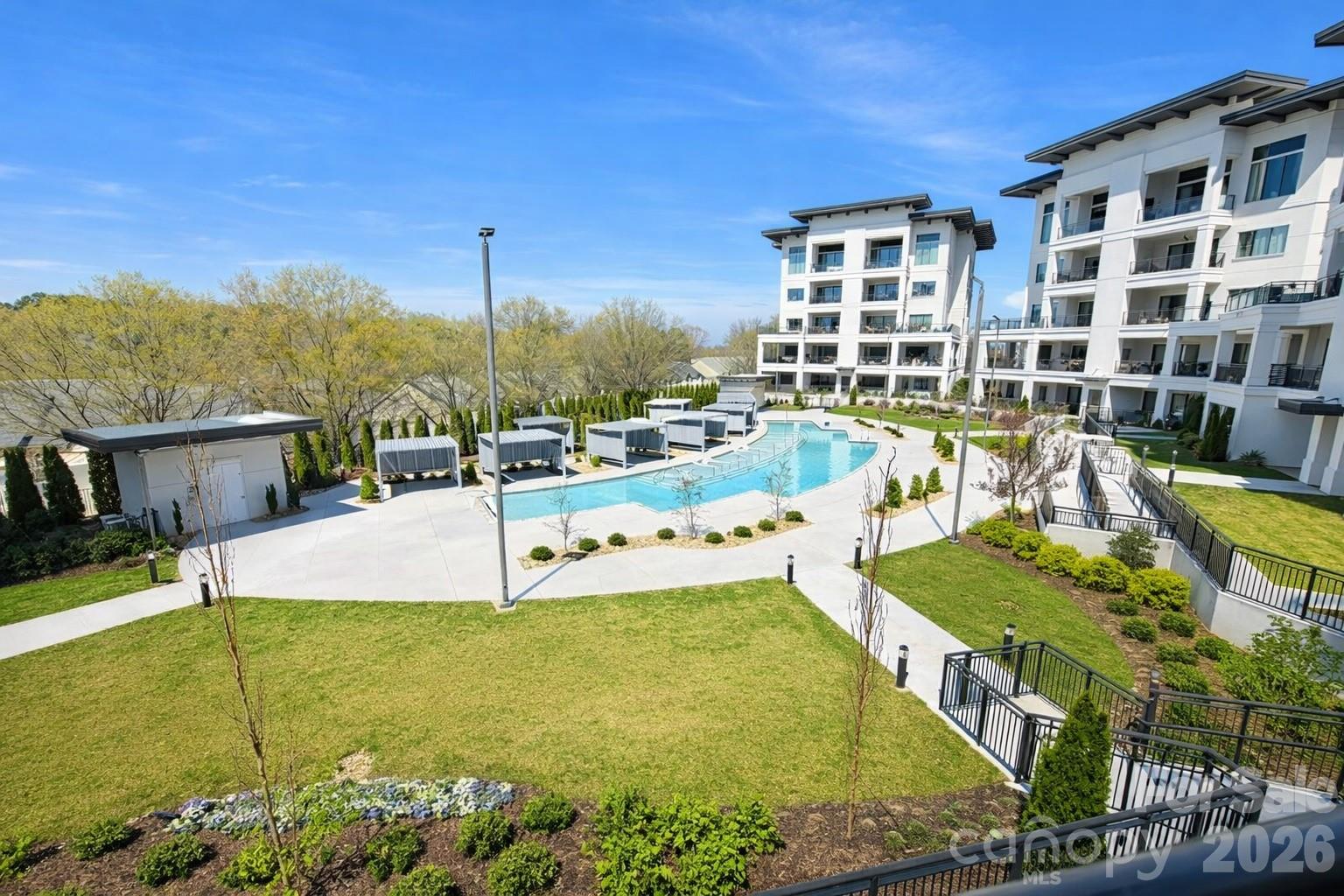 Condominium courtyard with a curved pool, cabanas, and modern white buildings.