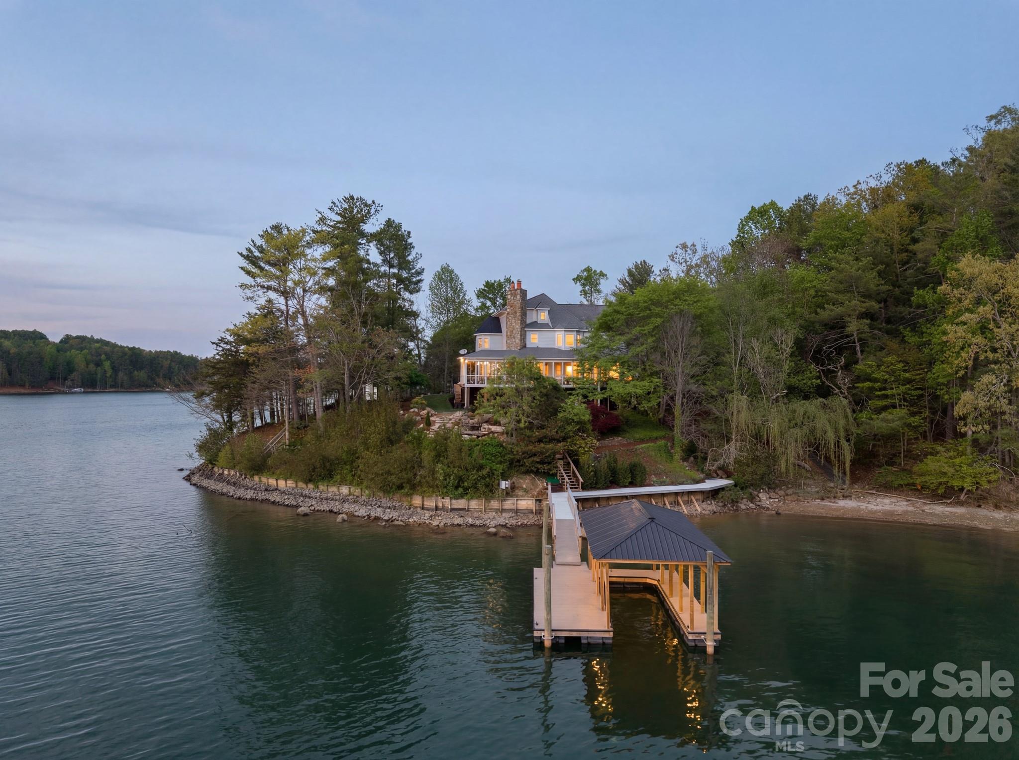 Lakefront home with a covered dock extending into the water at dusk.