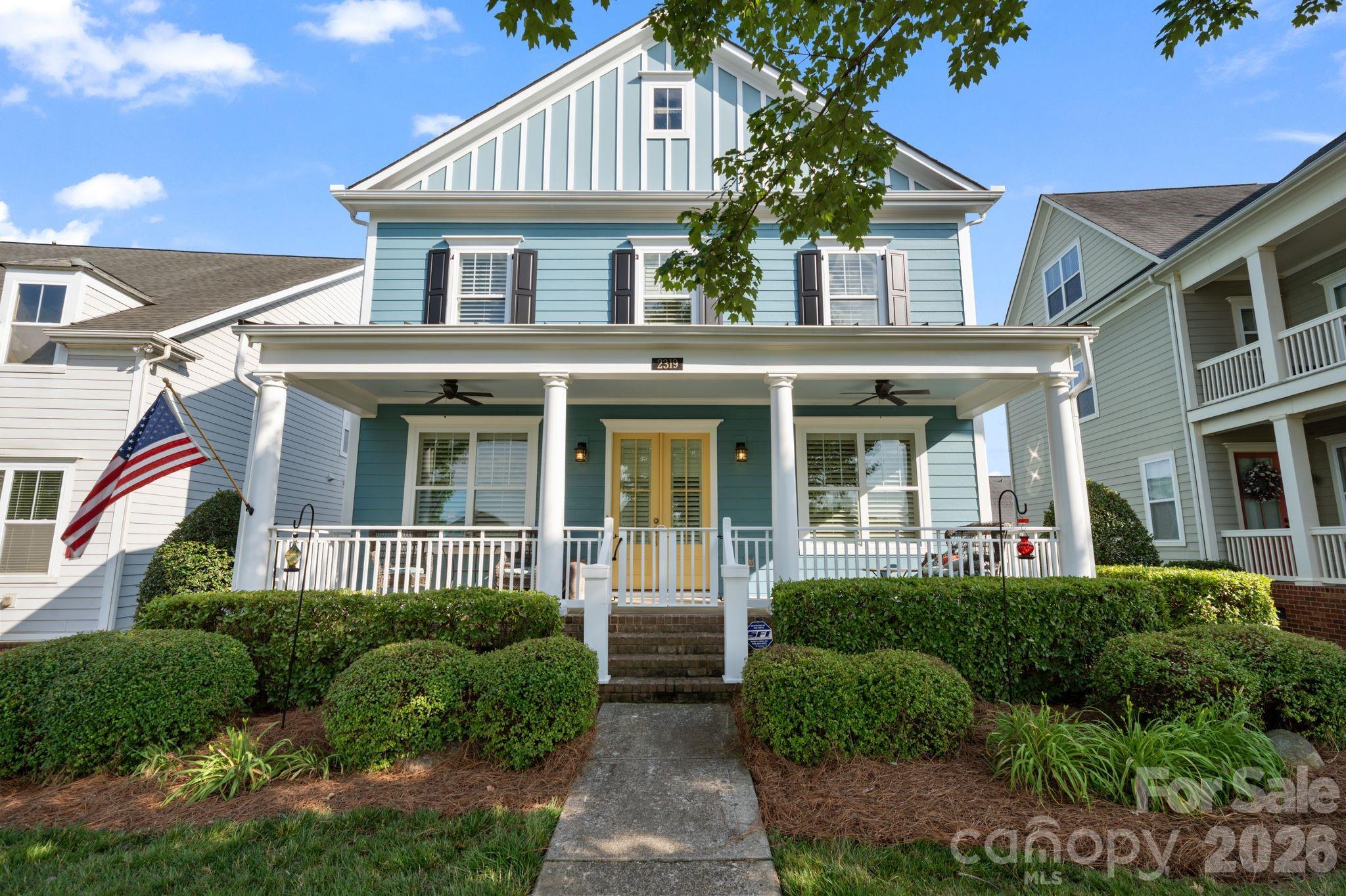 Blue two-story house with a columned front porch, yellow double doors, and an American flag.