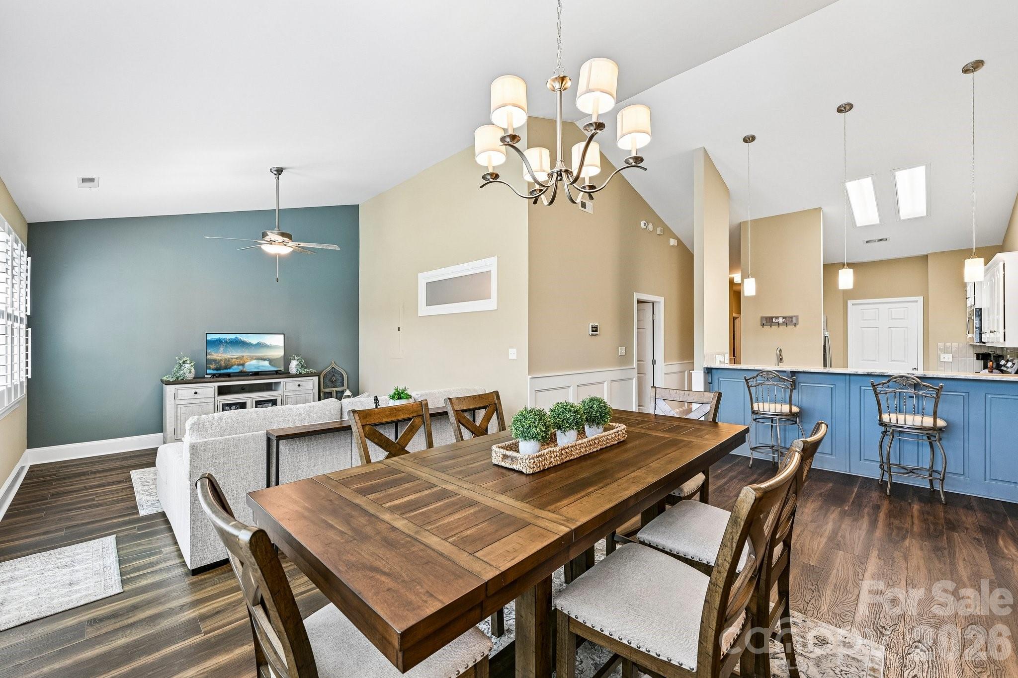 Open-plan condo dining and living area with a large wood table, blue kitchen island, and teal accent wall.