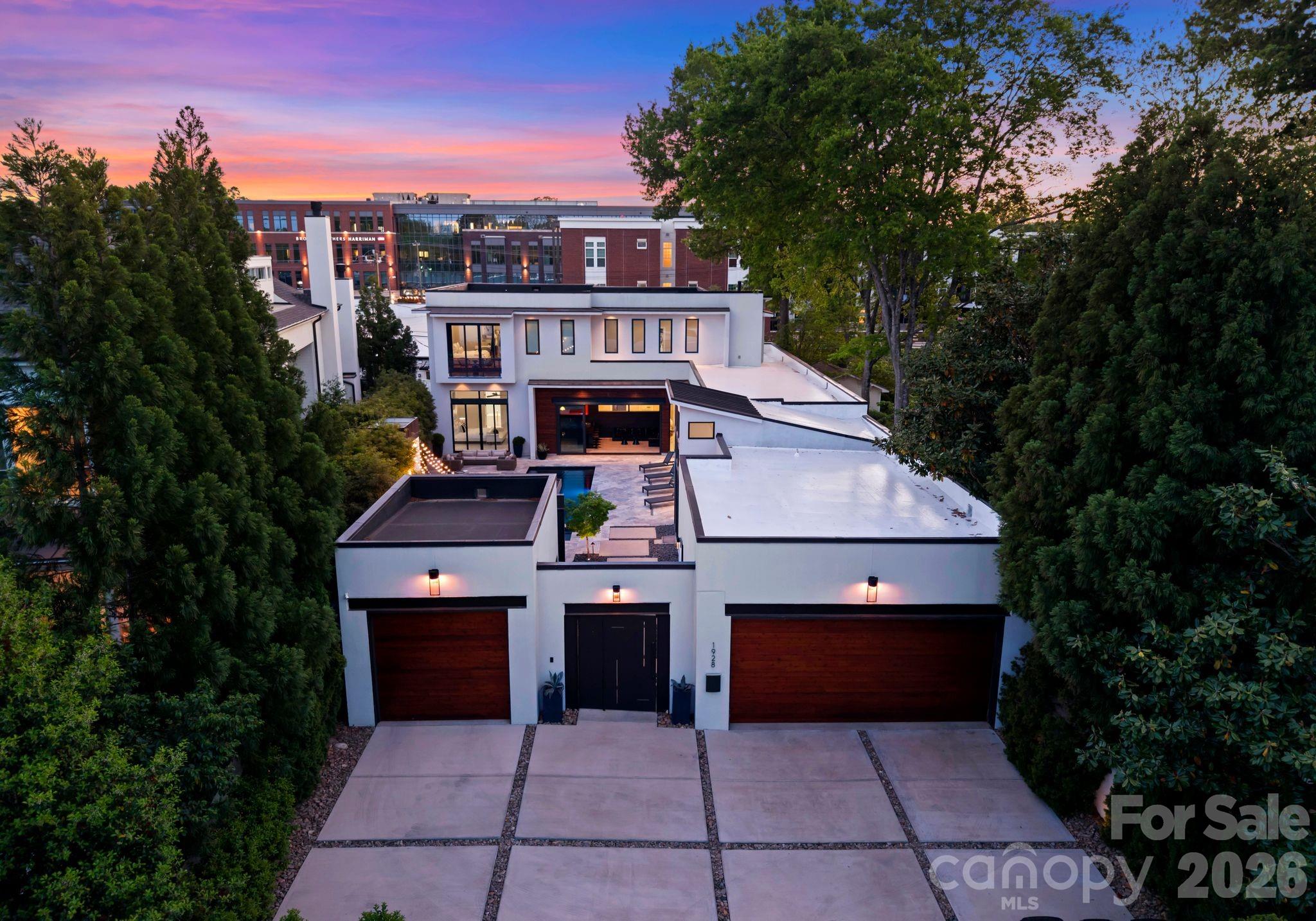 Modern white home with twin wood garage doors and rooftop terraces at dusk.