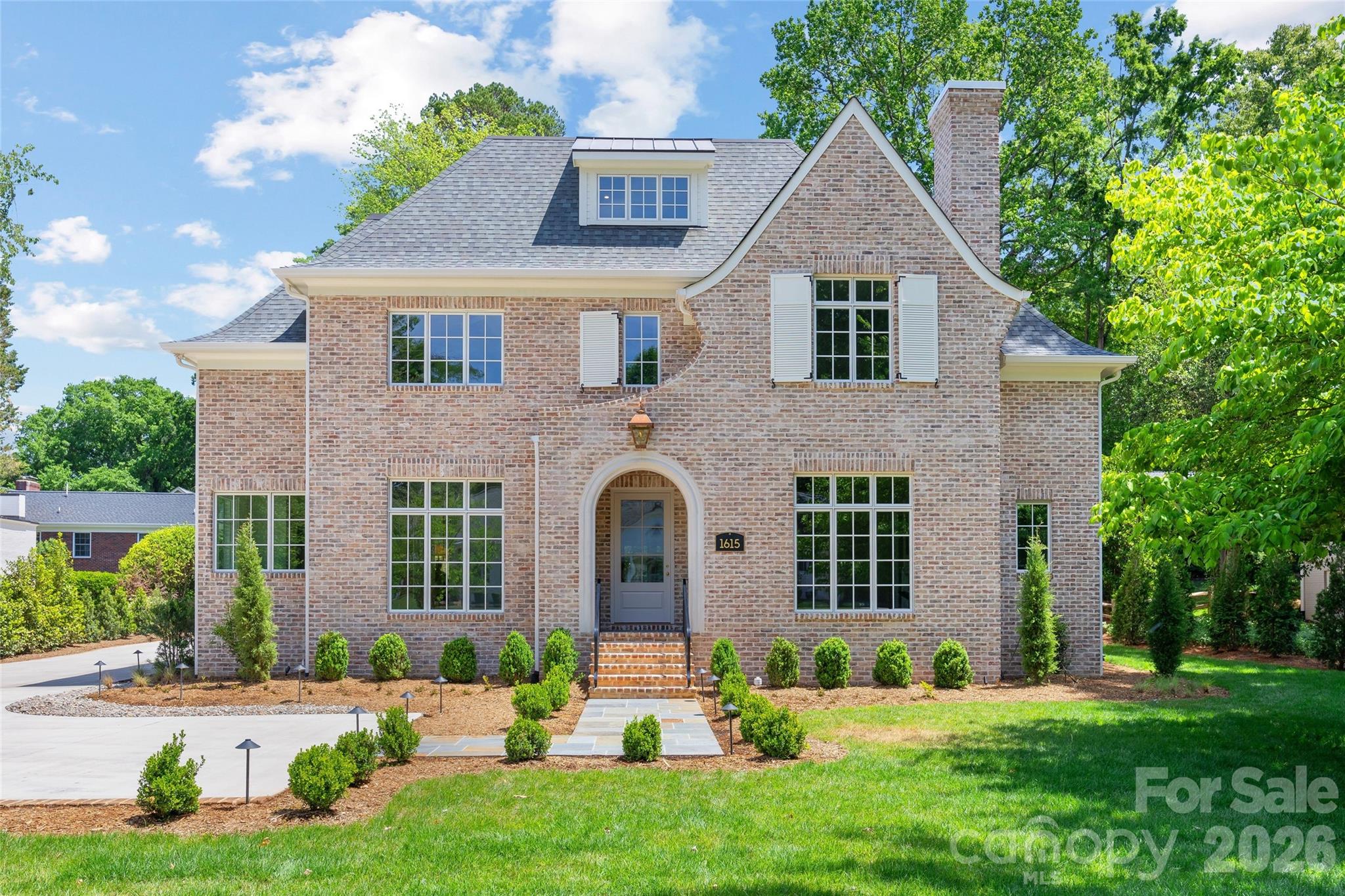 Two-story brick house with an arched entry, gray shingle roof, and landscaped front lawn.