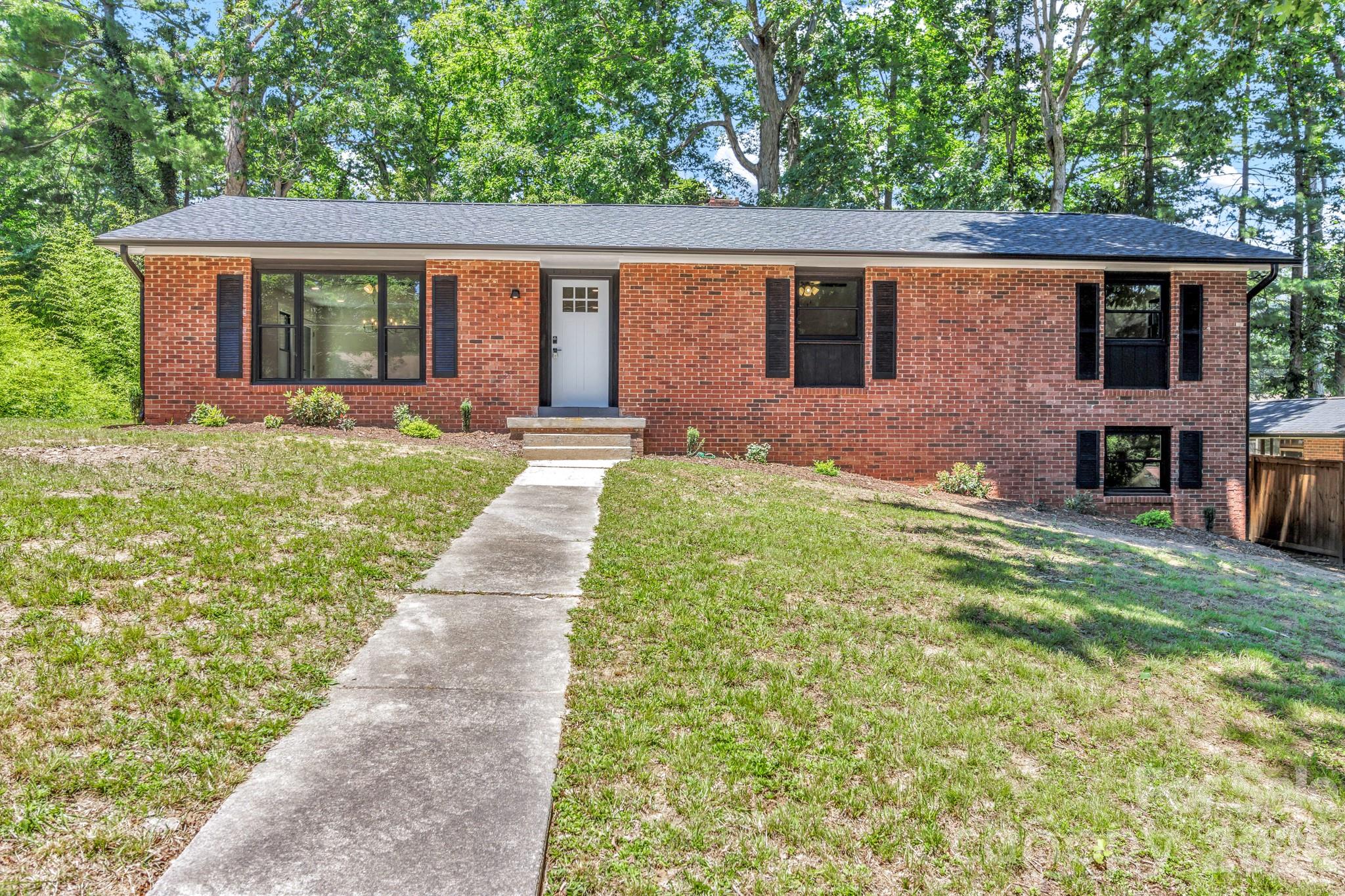 Red-brick home with black shutters, a white front door, and a walkway through the lawn.