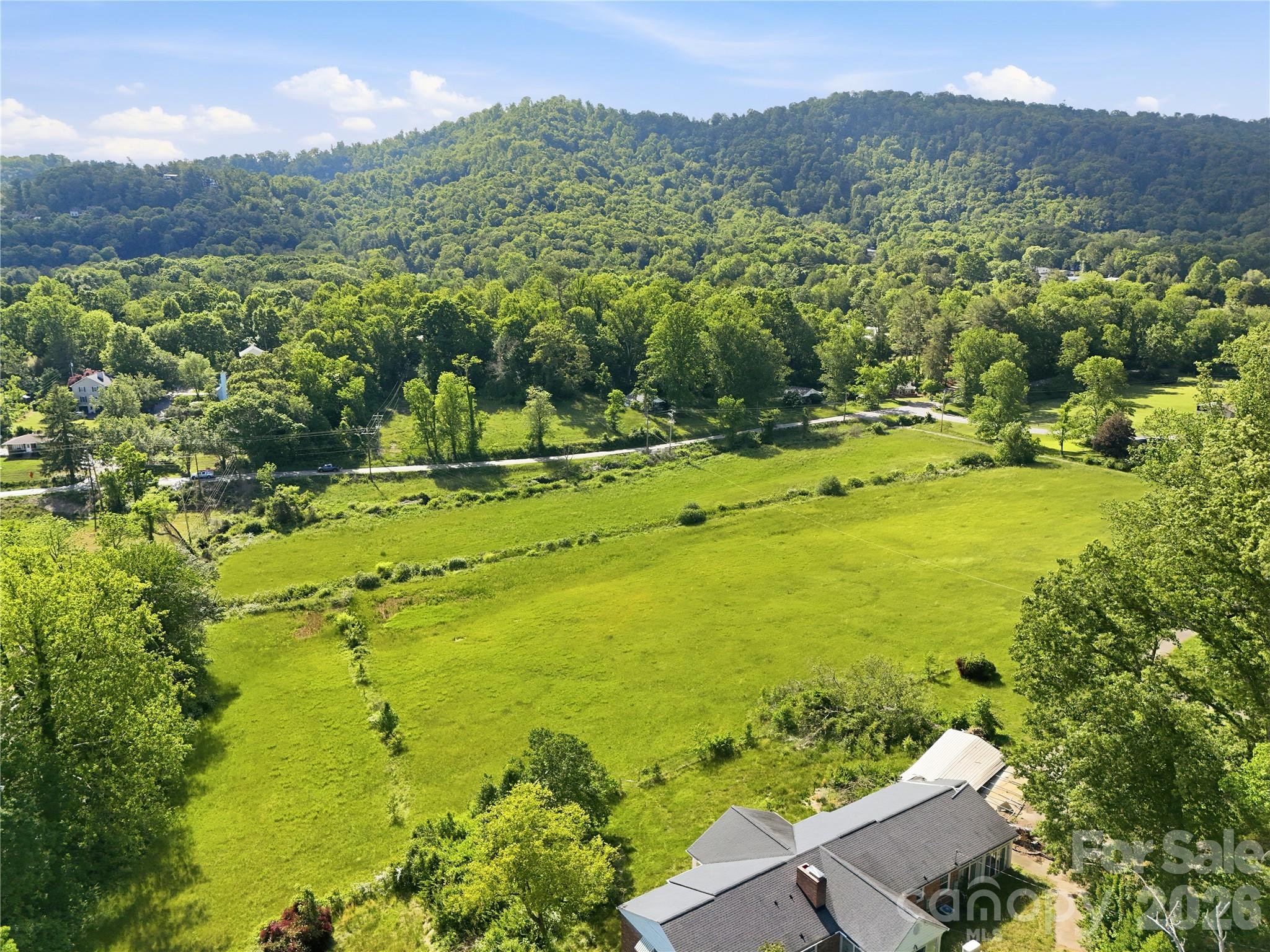 Aerial view of a green meadow, scattered homes, and wooded hills, with a house in the foreground.