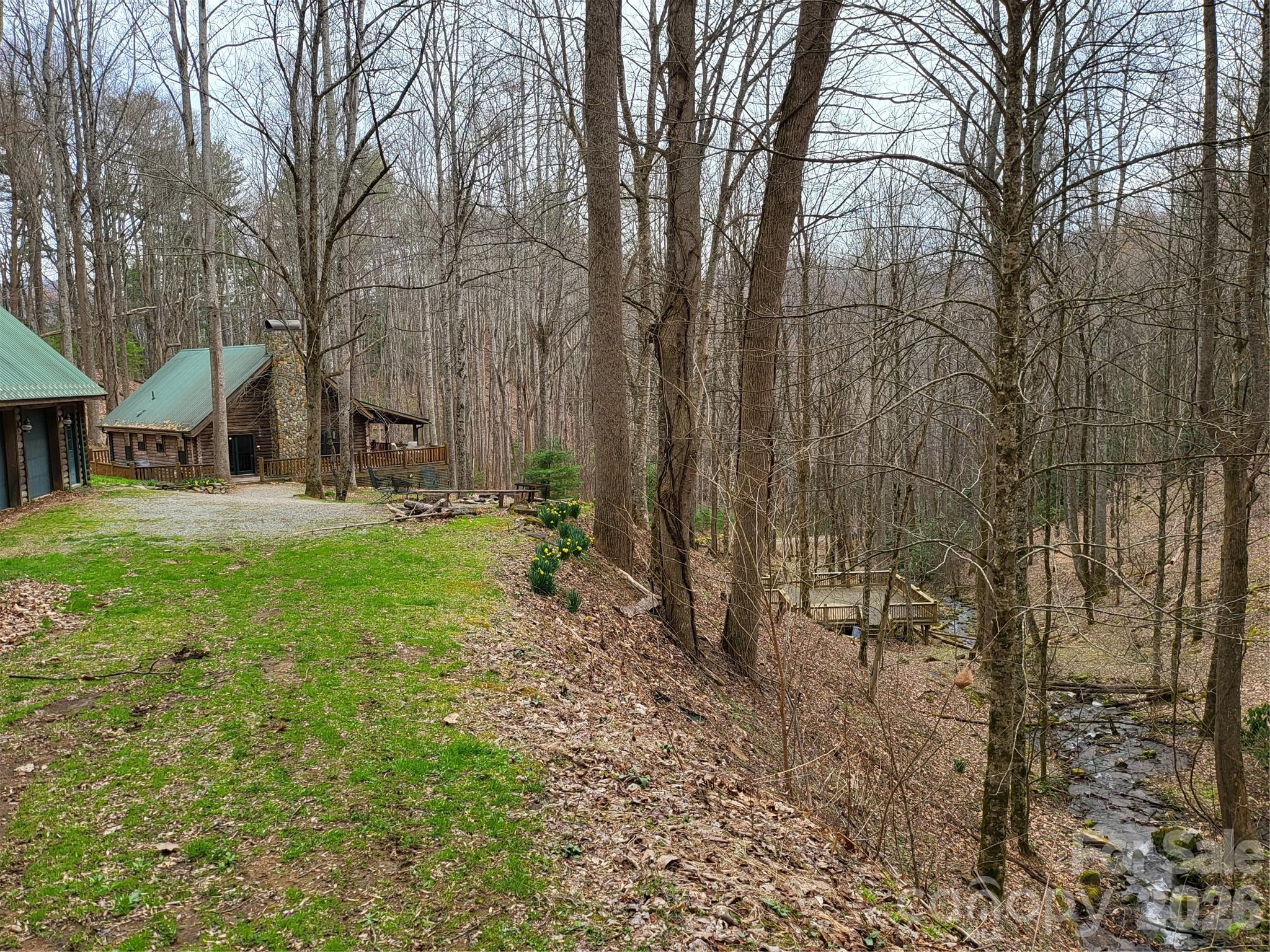 Rustic log cabins on a wooded hillside beside a creek, with green metal roofs and a gravel drive.