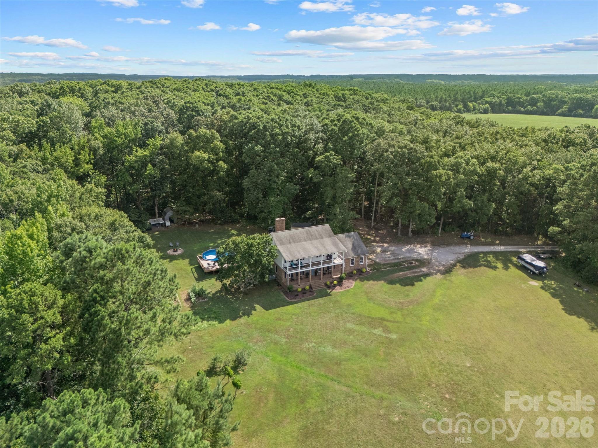 Aerial view of a brick house, spacious lawn, above-ground pool, and surrounding forest.