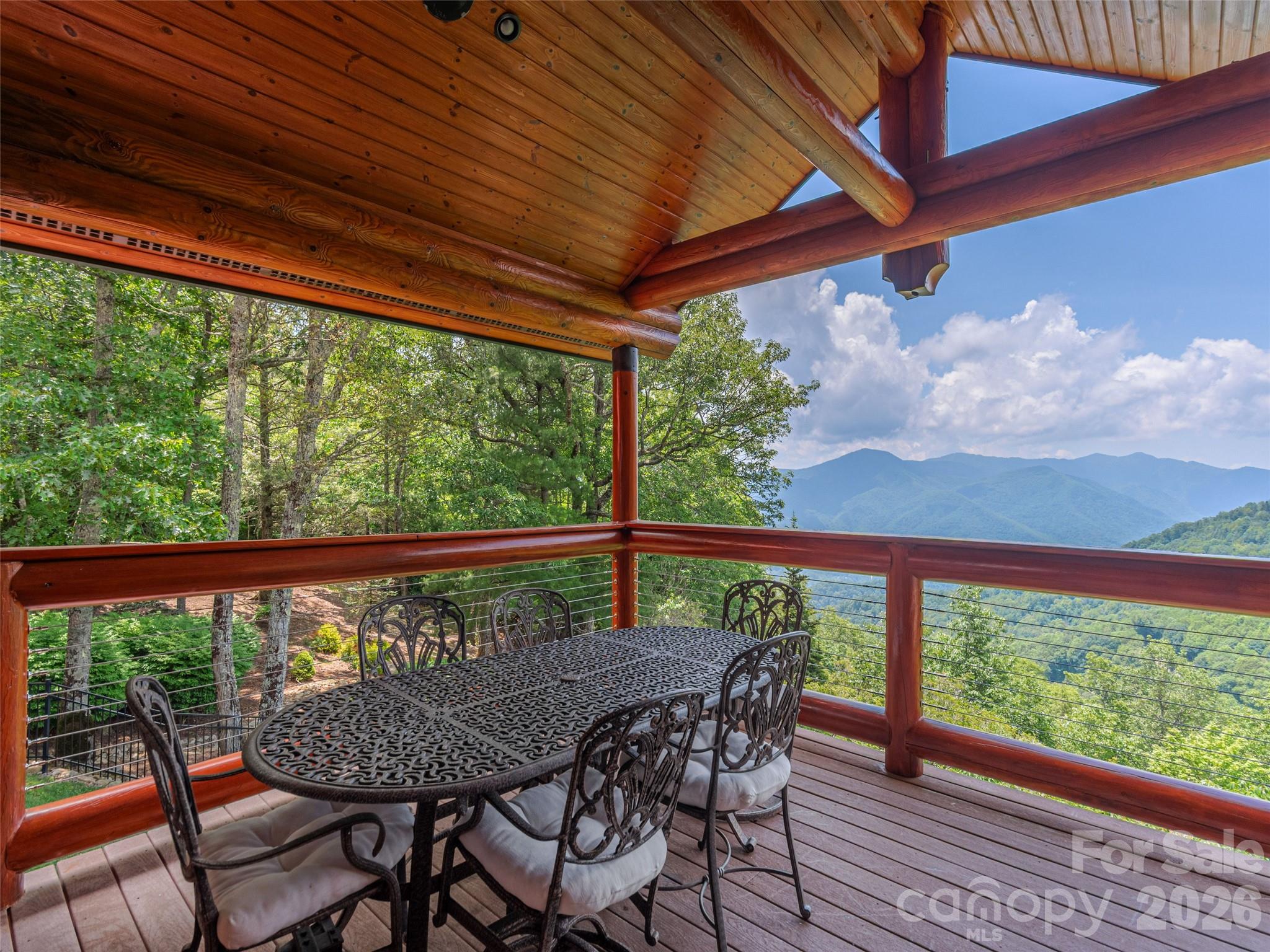 Covered mountain-view deck with a wooden canopy and wrought-iron dining set.