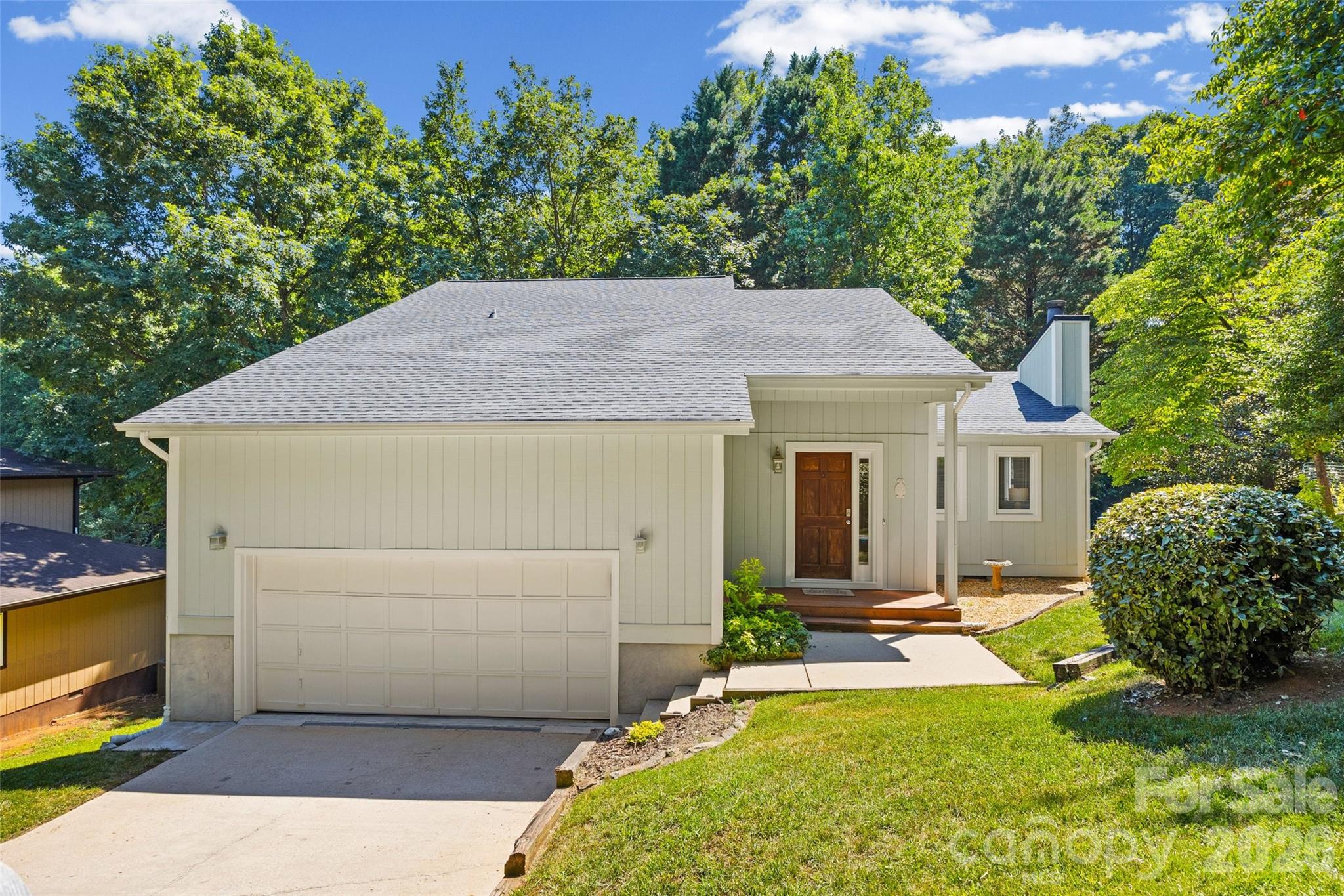 Light-colored home with a large attached garage, covered entry, and mature trees.